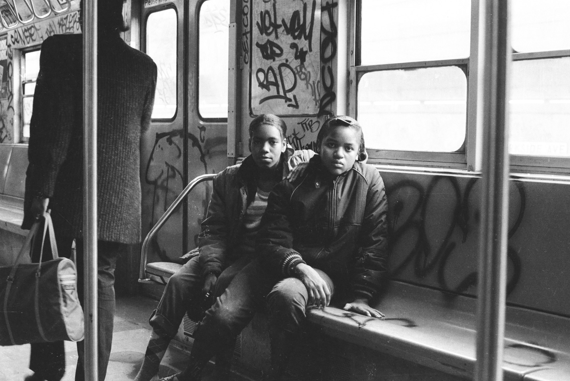 Two young girls posing for a portrait on the subway in 1980.