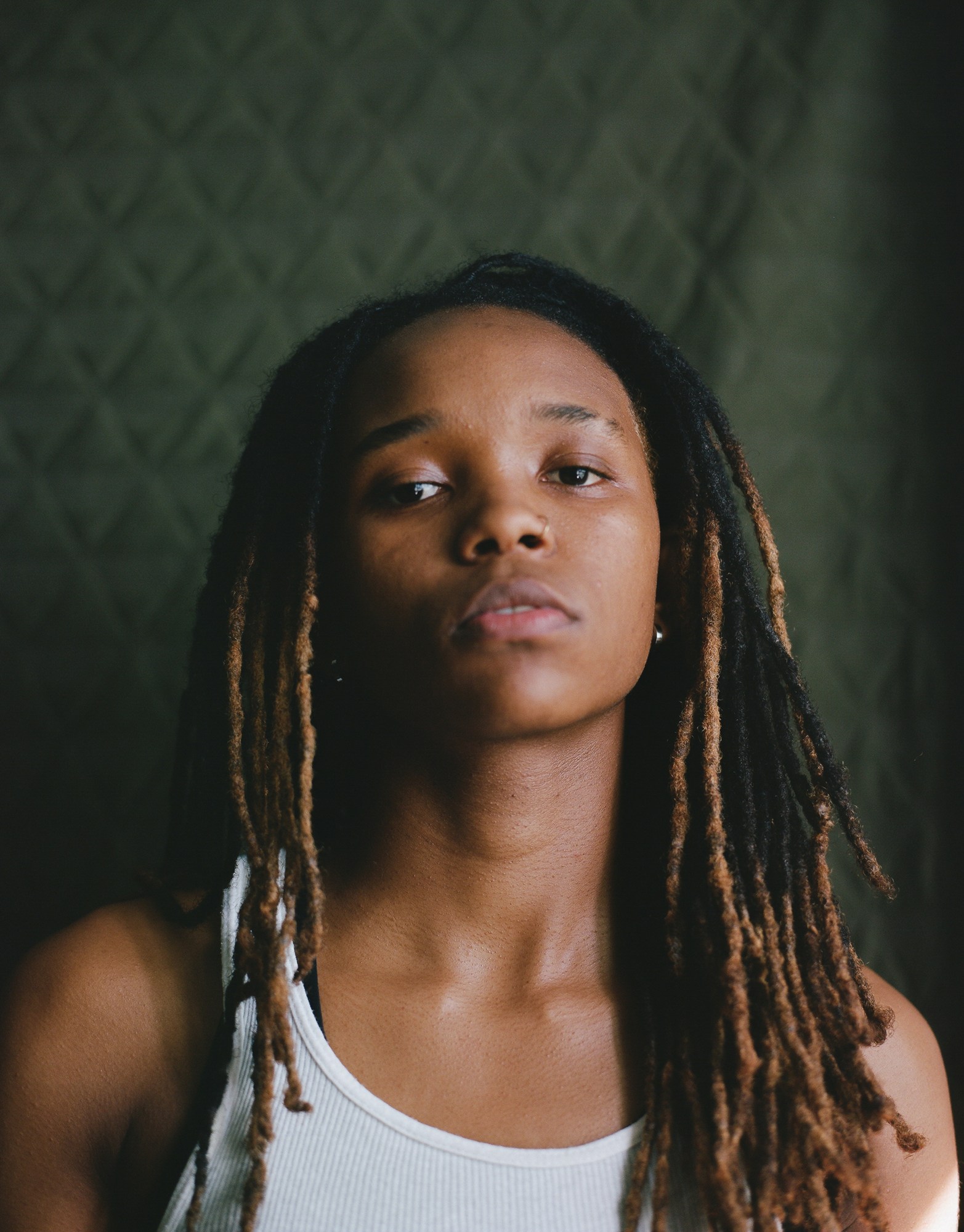 a model with long dreadlocks wearing a white vest looks to the camera