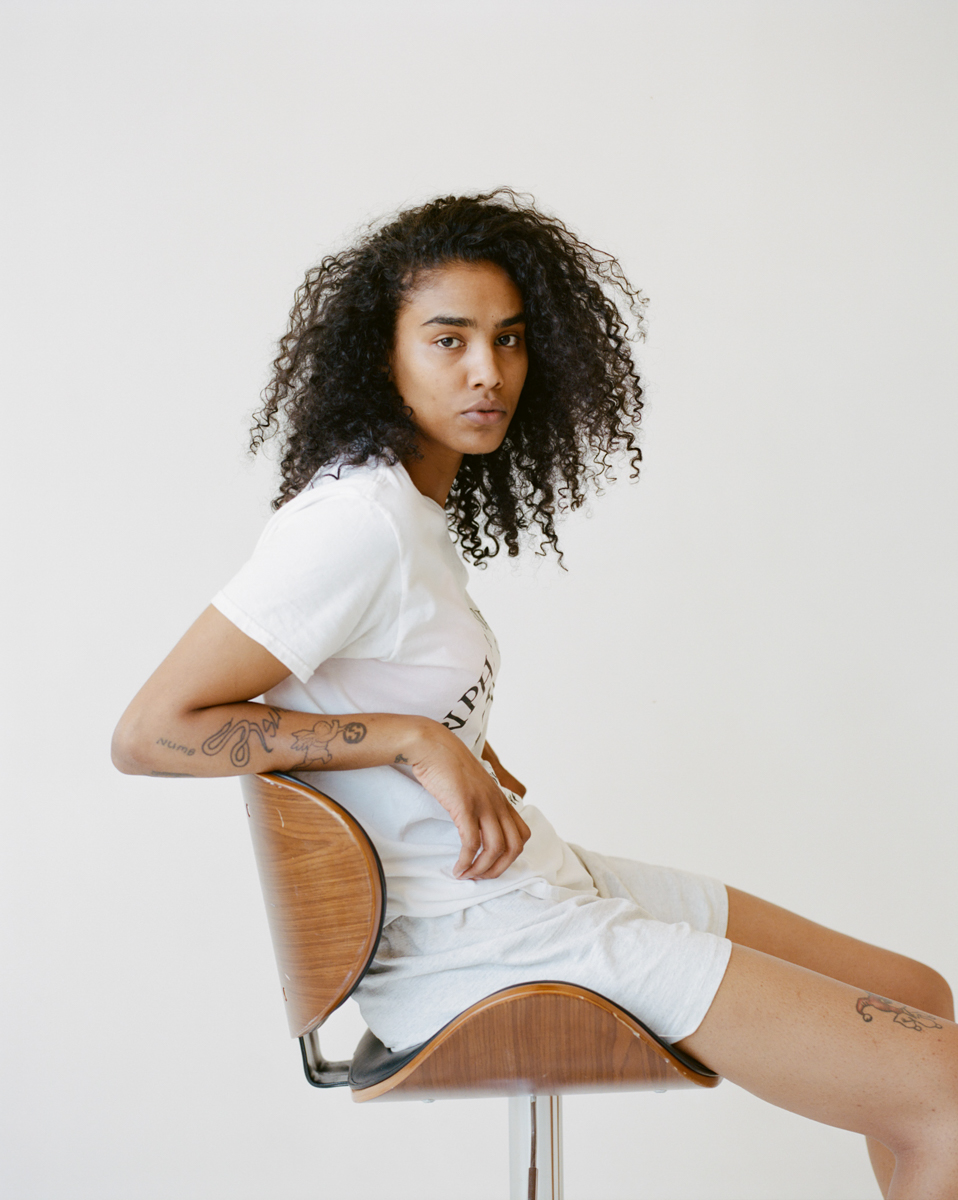 model dressed in white poses in a wood chair in front of a white background