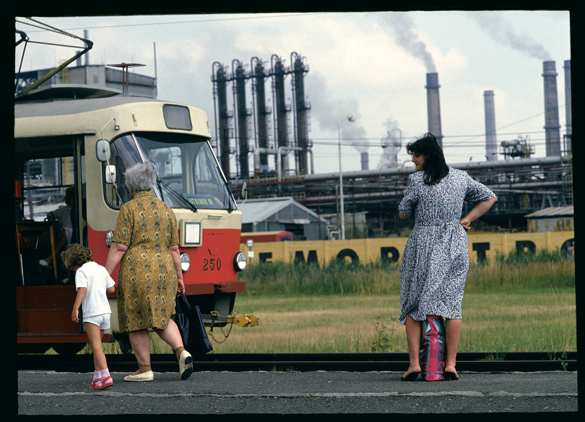 An elderly woman holding a young child's hand in front of a train.