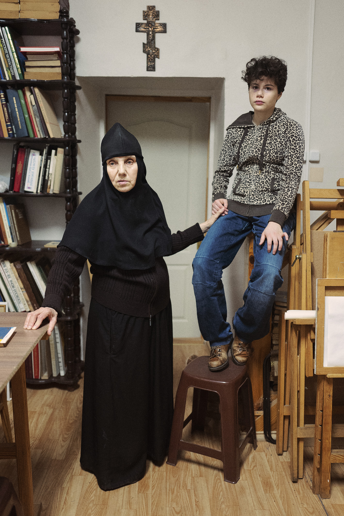 A young boy sitting with a nun in a library.