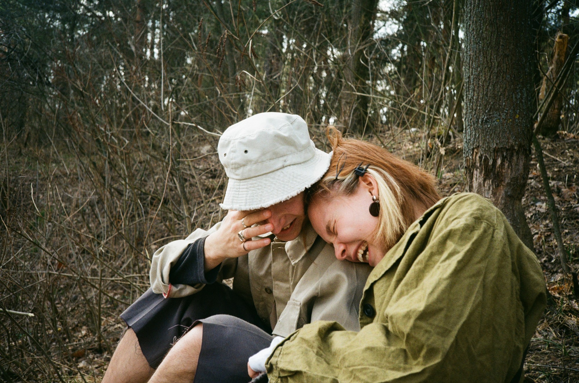 A couple laughing together sitting on a clearing in the woods.