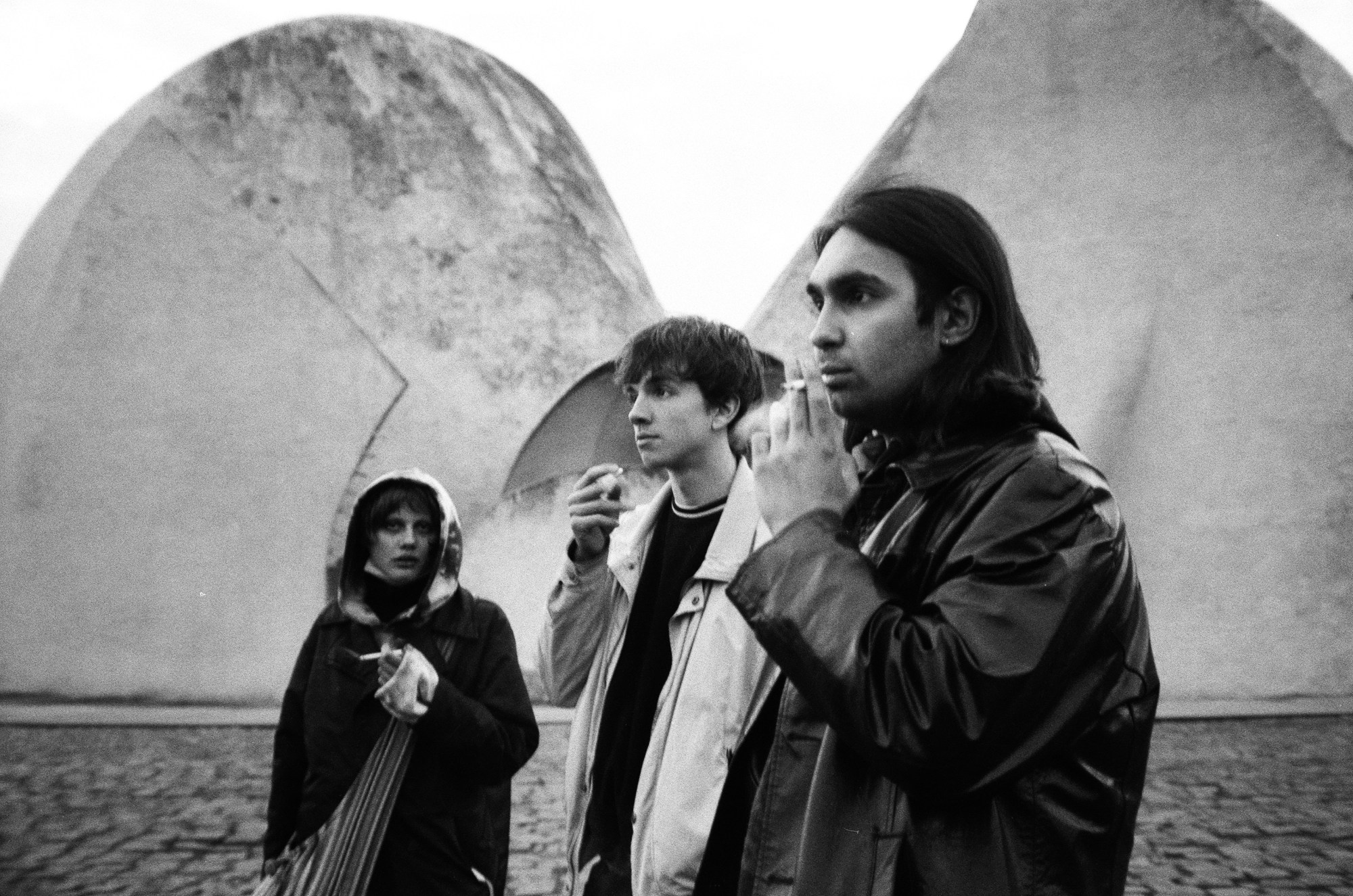 Three friends smoking cigarettes near a large concrete structure in Ukraine.