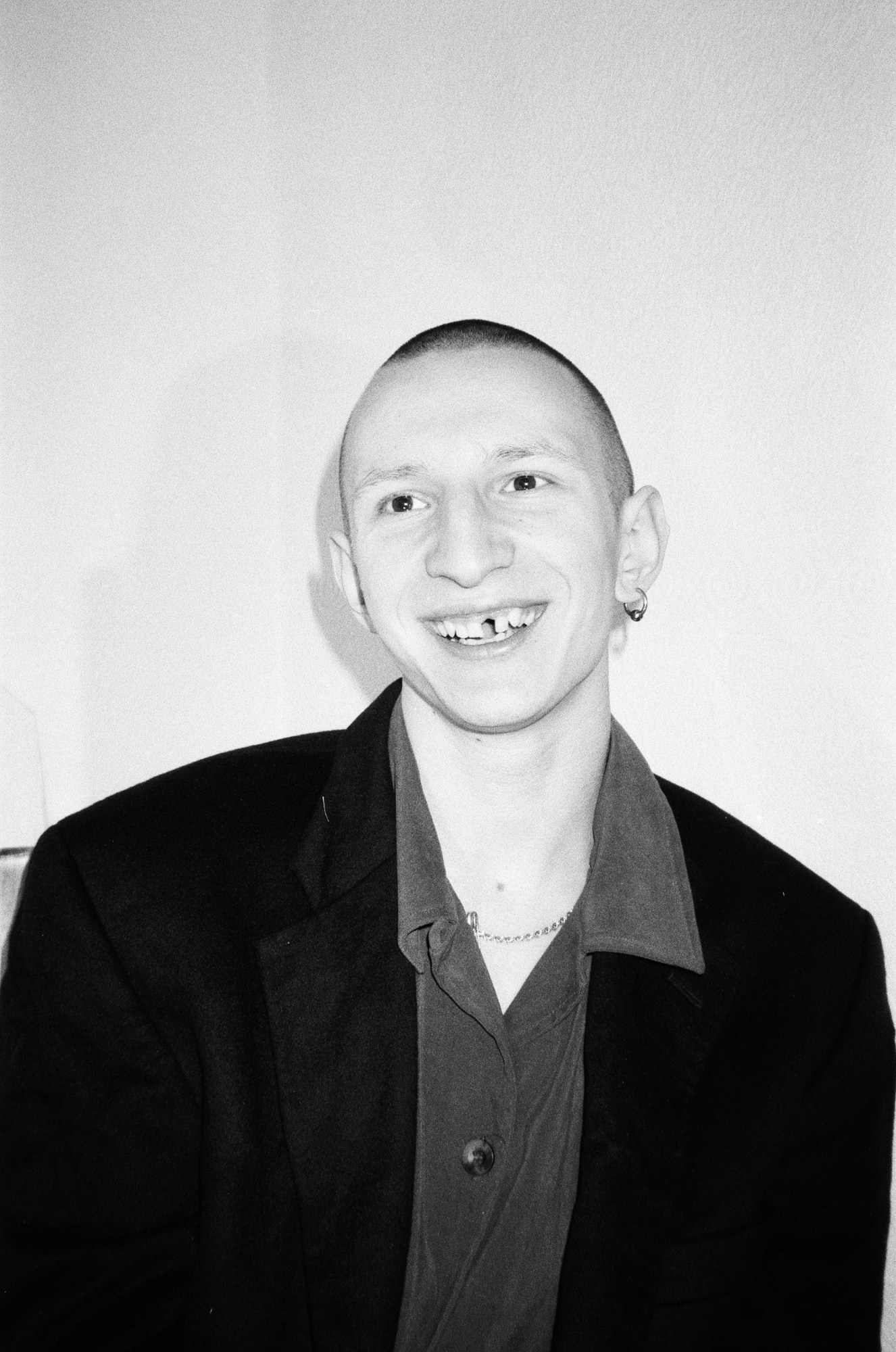 A man with a missing tooth and silver earring smiling for a portrait.