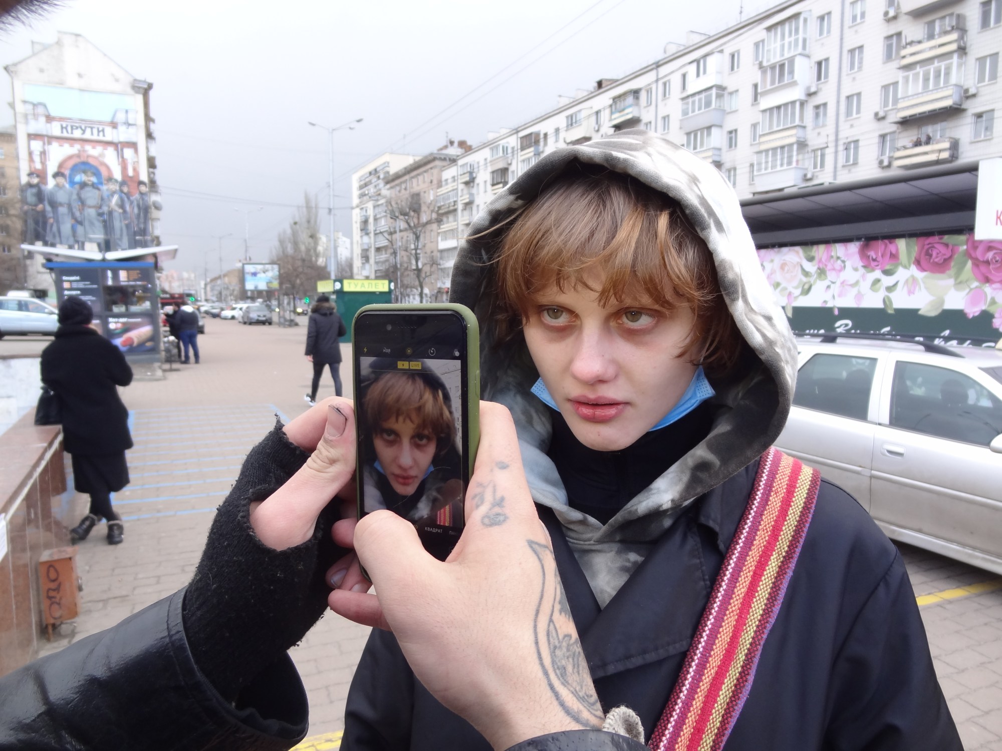 A woman being photographed by a man with one fingerless glove in a parking lot.