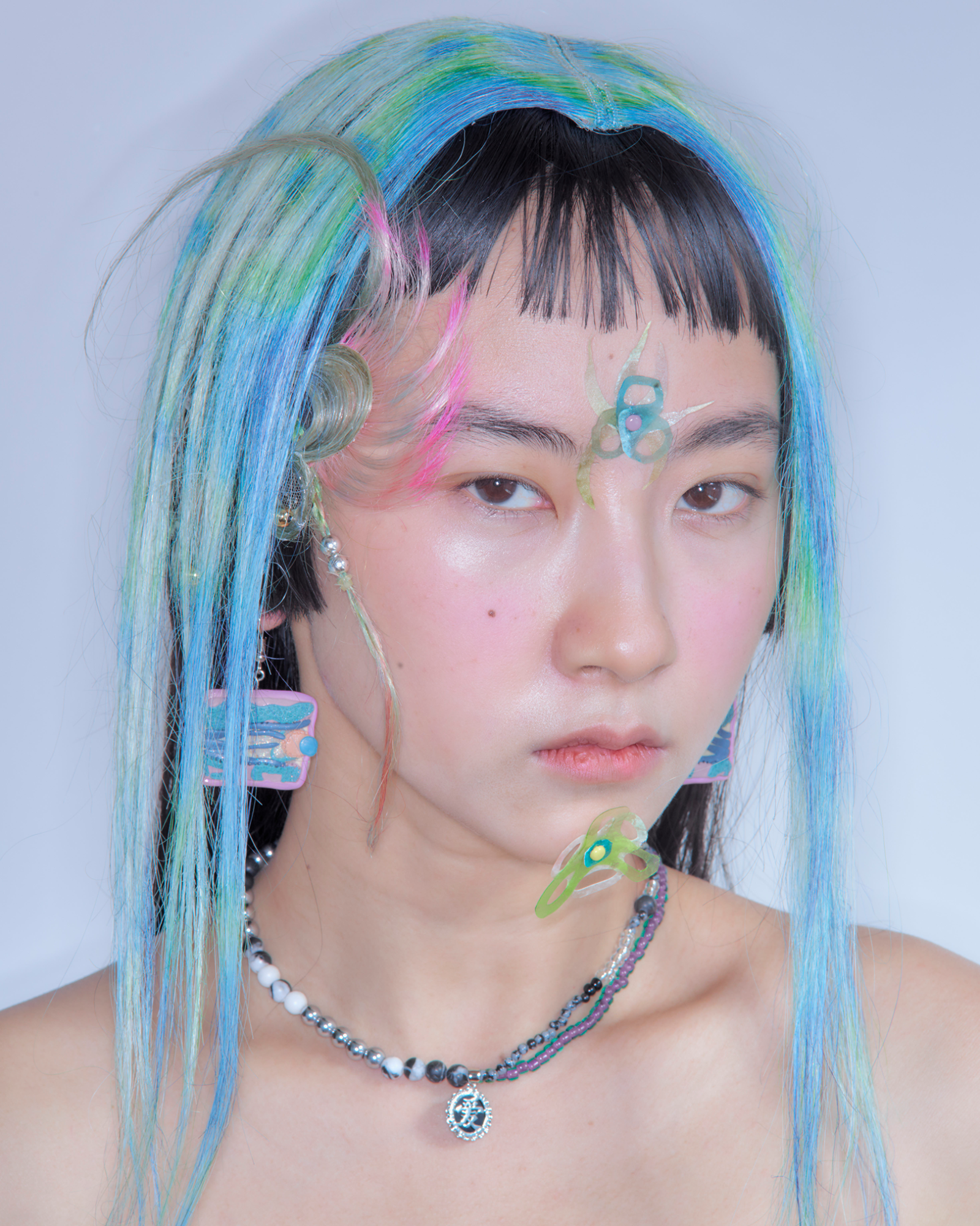 a model wears an icy blue and green hairpiece, with their own short black fringe underneath