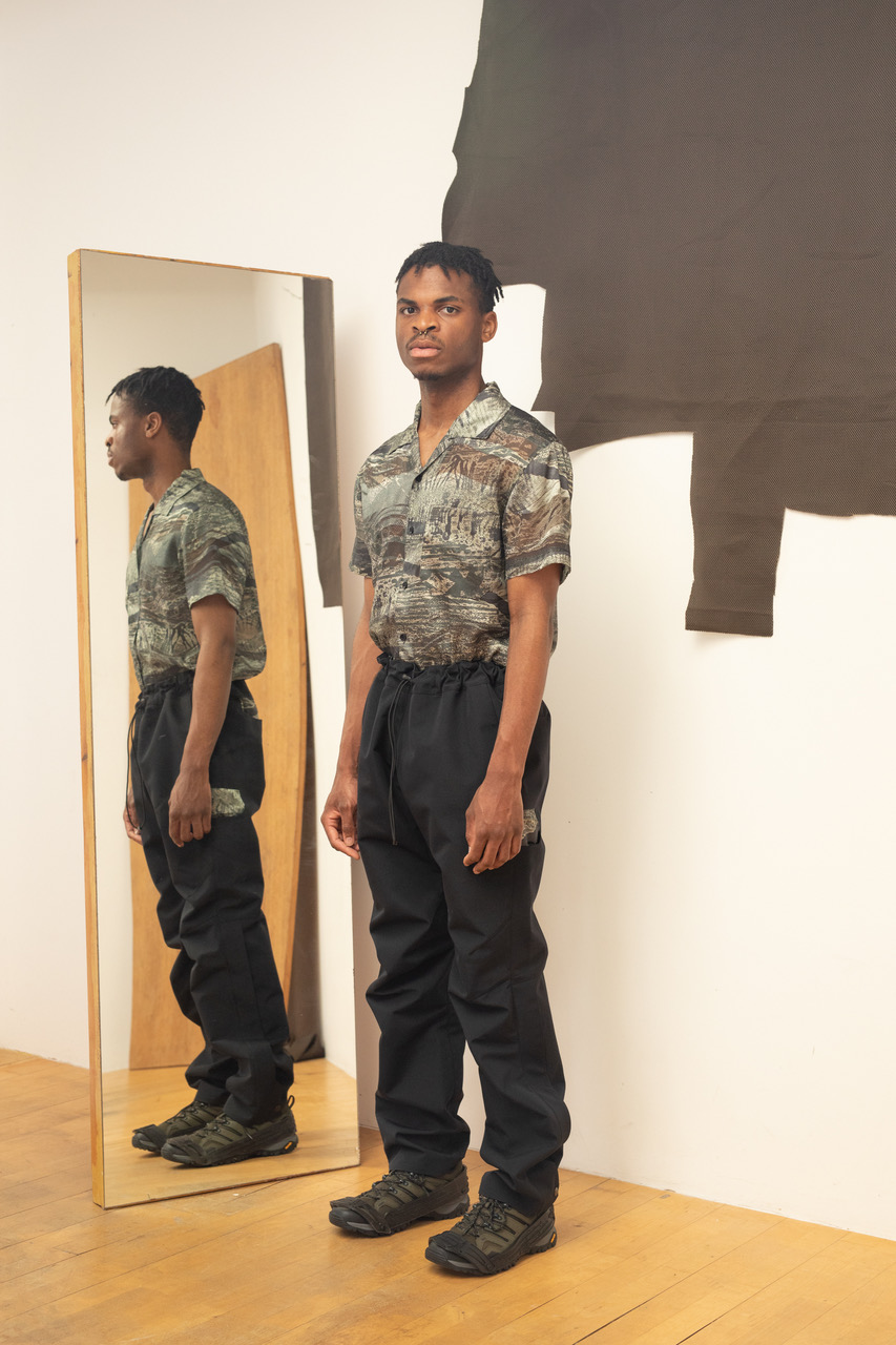 A model wearing a camo-shirt and black Gore-Tex trousers from Olly Shinder's CSM graduate collection