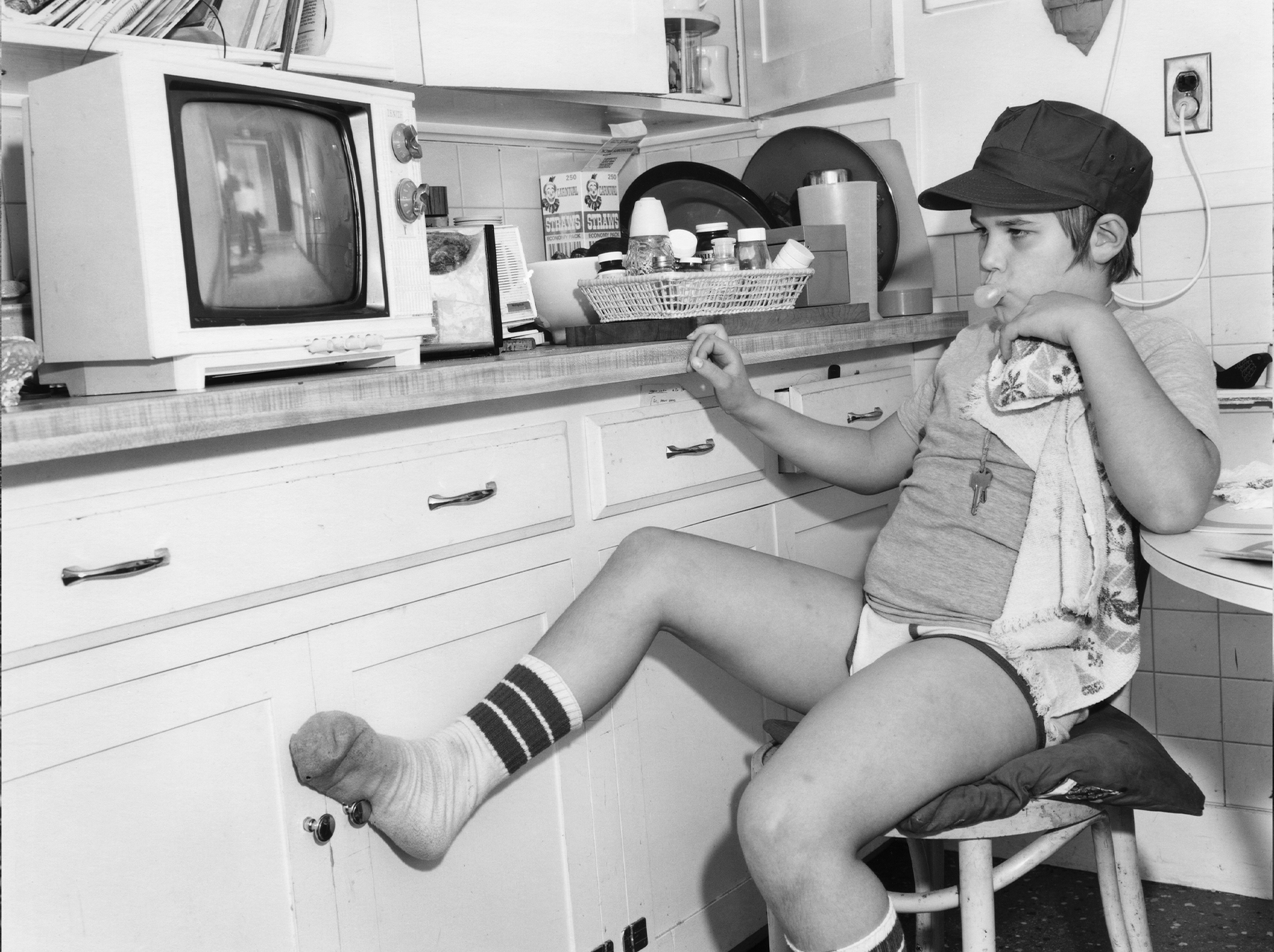 a young model sits askew on a kitchen stool, blowing bubblegum