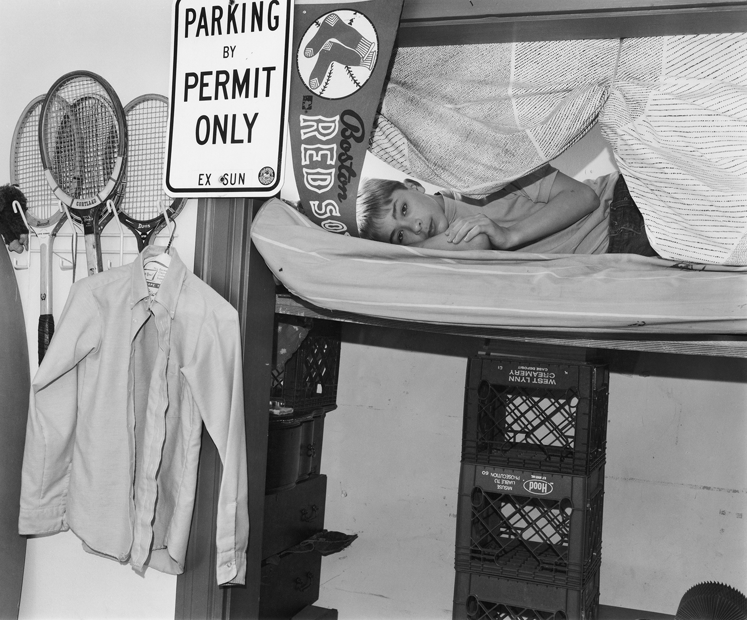 a young model lies in the top bunk of a bunk bed, surrounded by tennis rackets and other paraphenalia