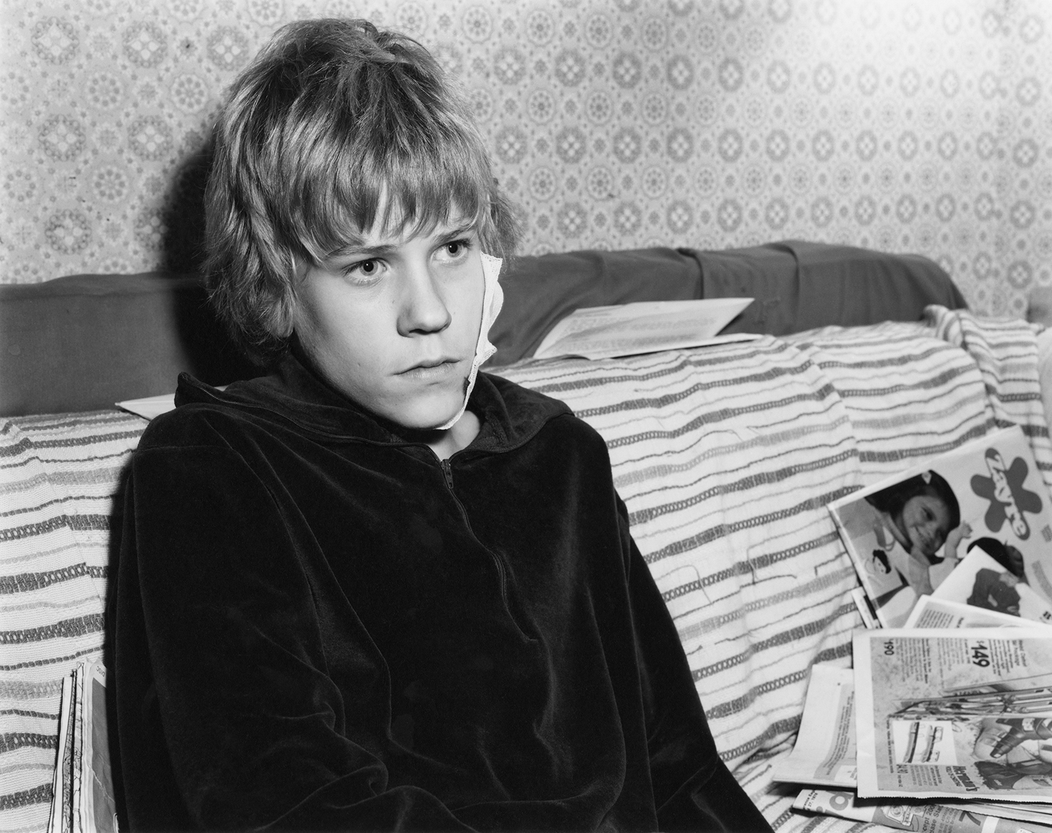 a young model with a large bandage on his cheek looks at something off frame