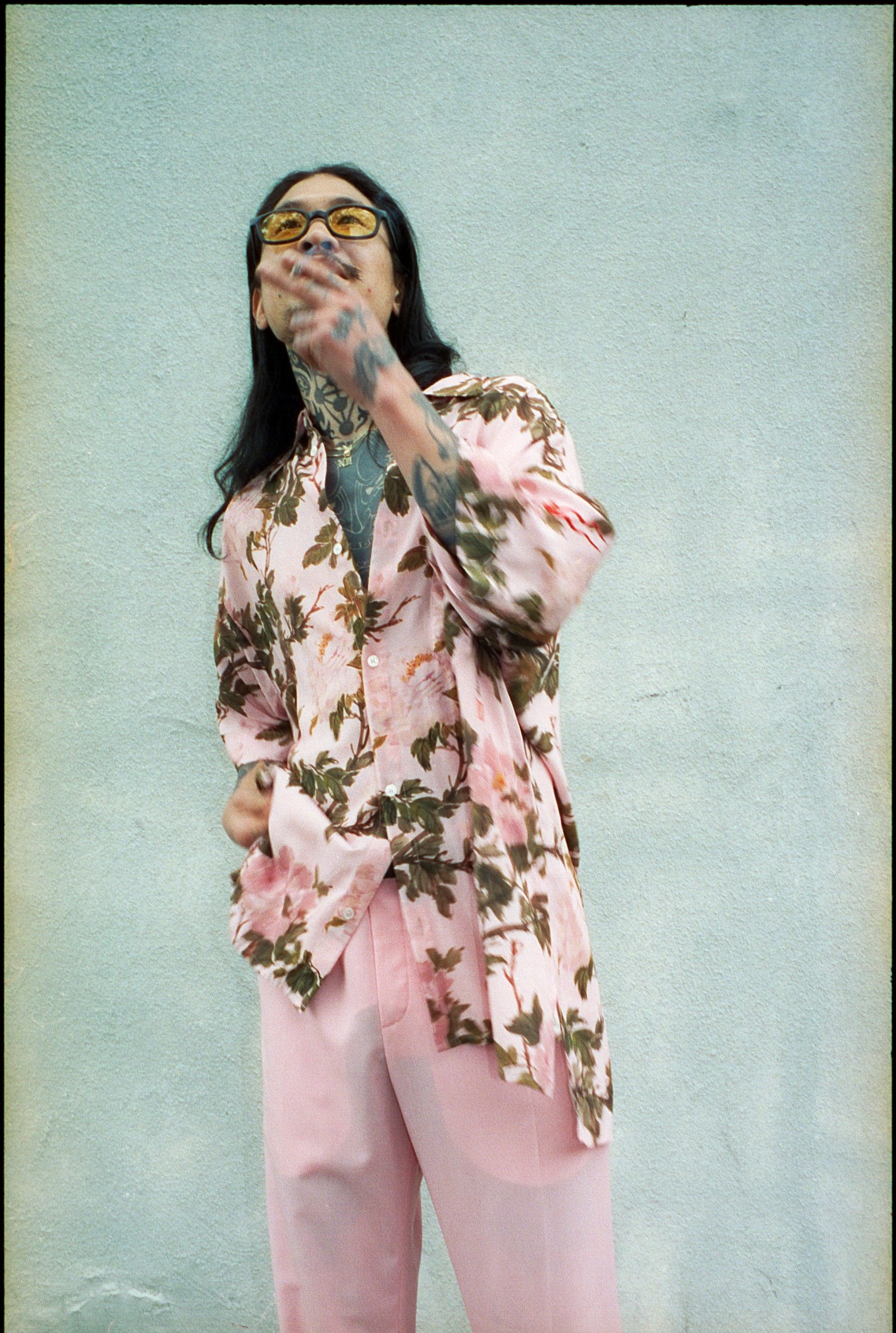 jae kim wearing a pink floral shirt and sunglasses in front of a blue wall