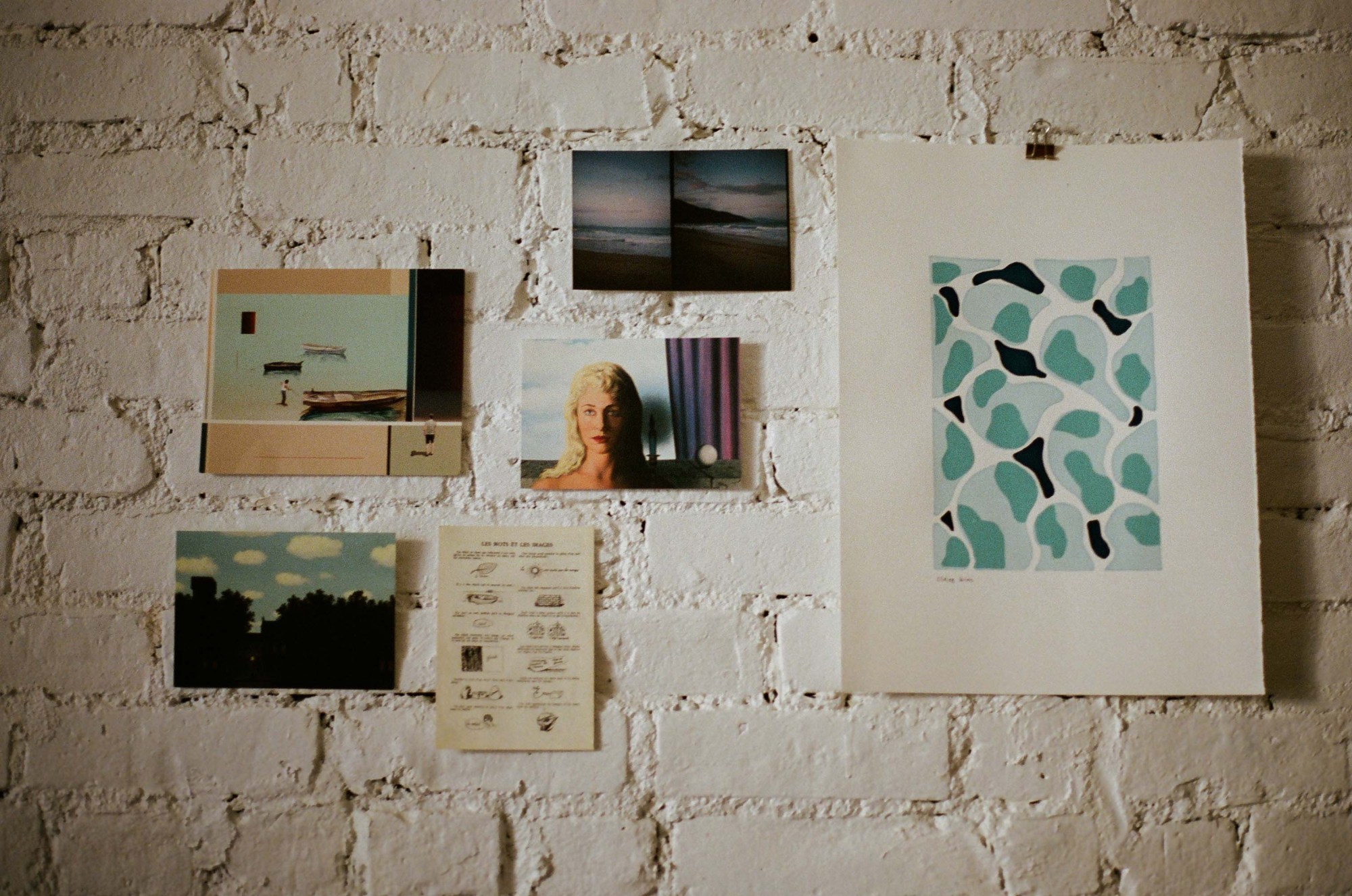 a photo of postcards and artwork hanging up on a white brick wall