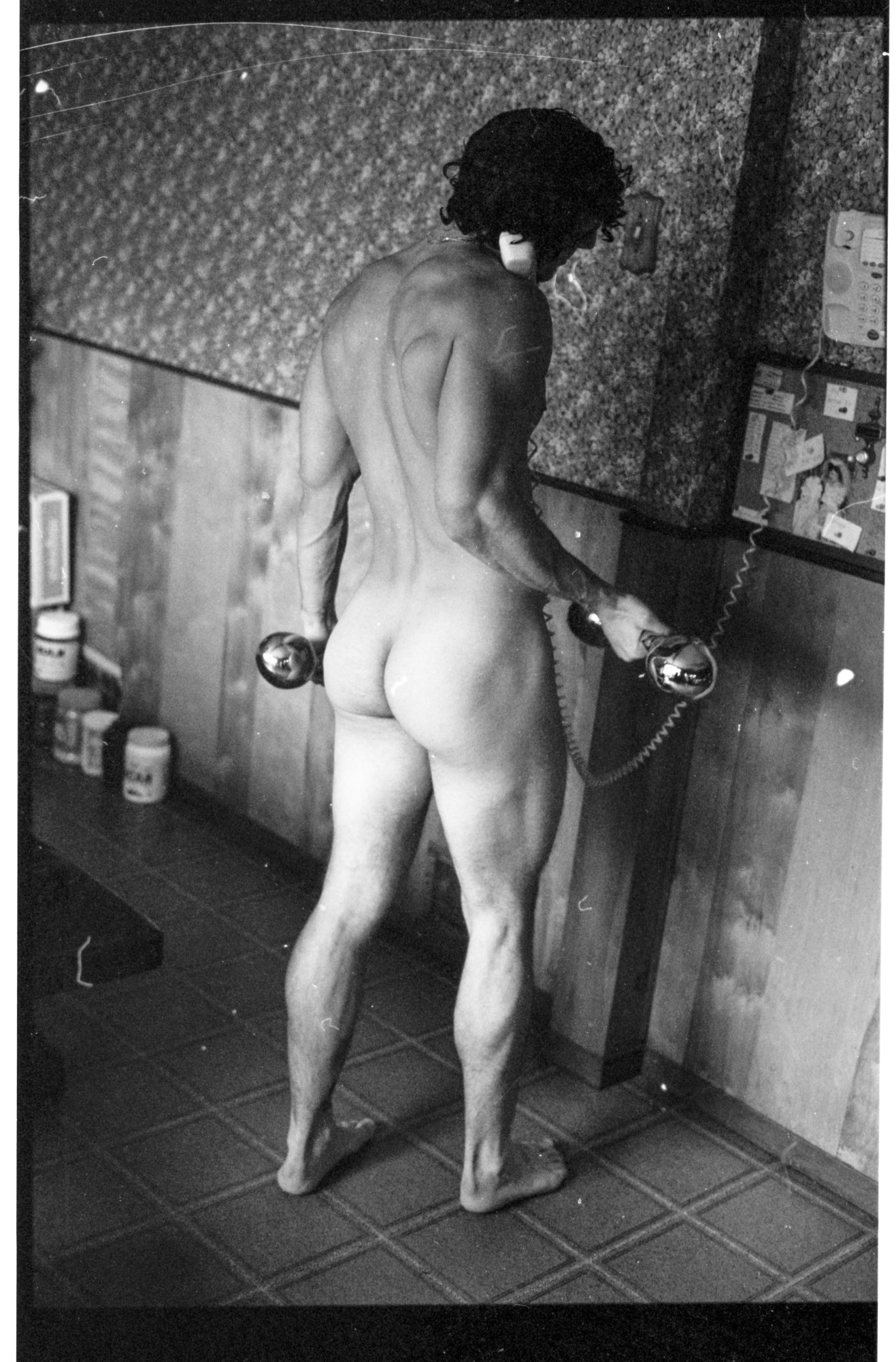 naked man holding a dumbbell while on the phone.