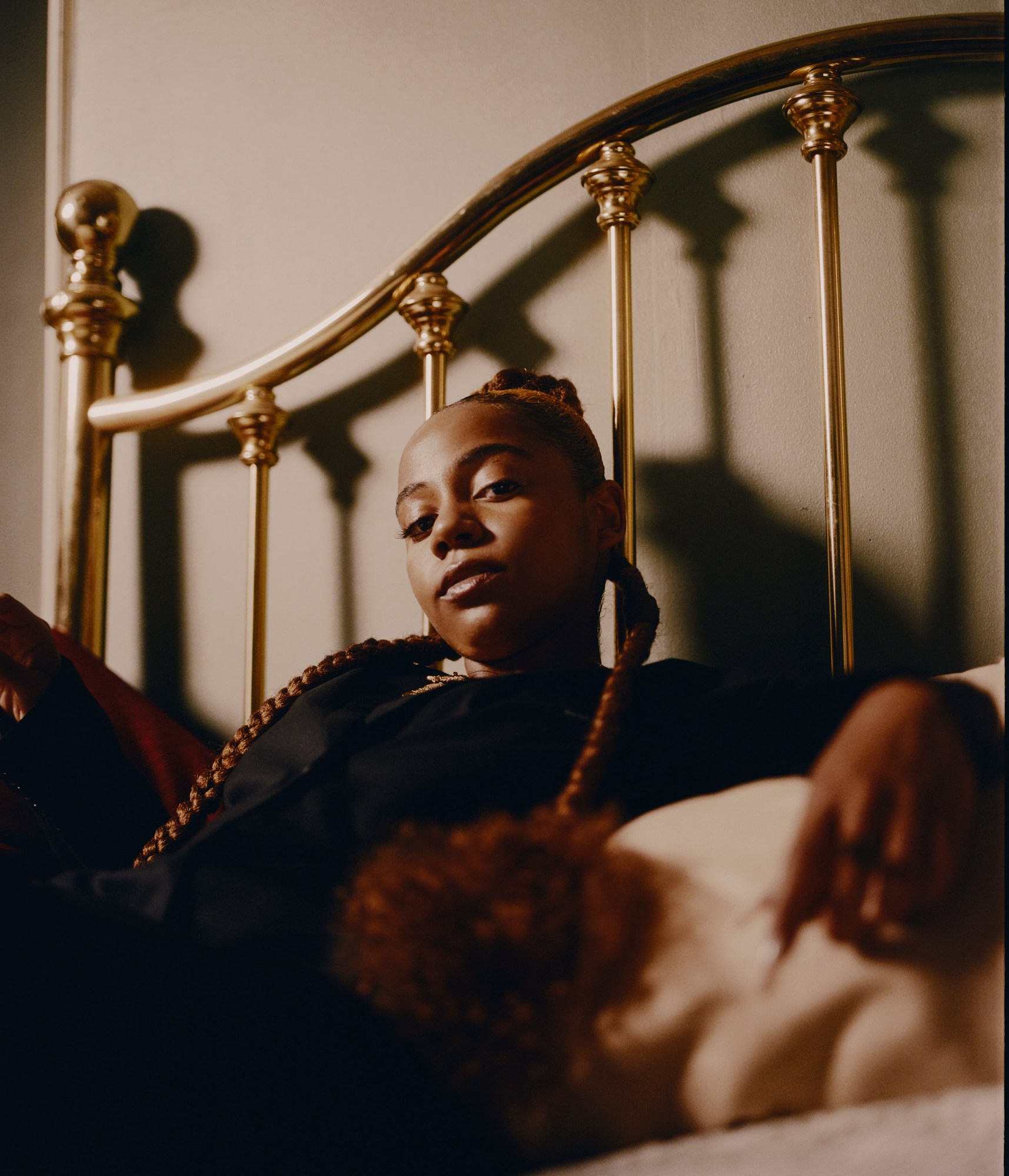 a girl with long braids sitting on a bed photographed by kendall bessent for chucha studios