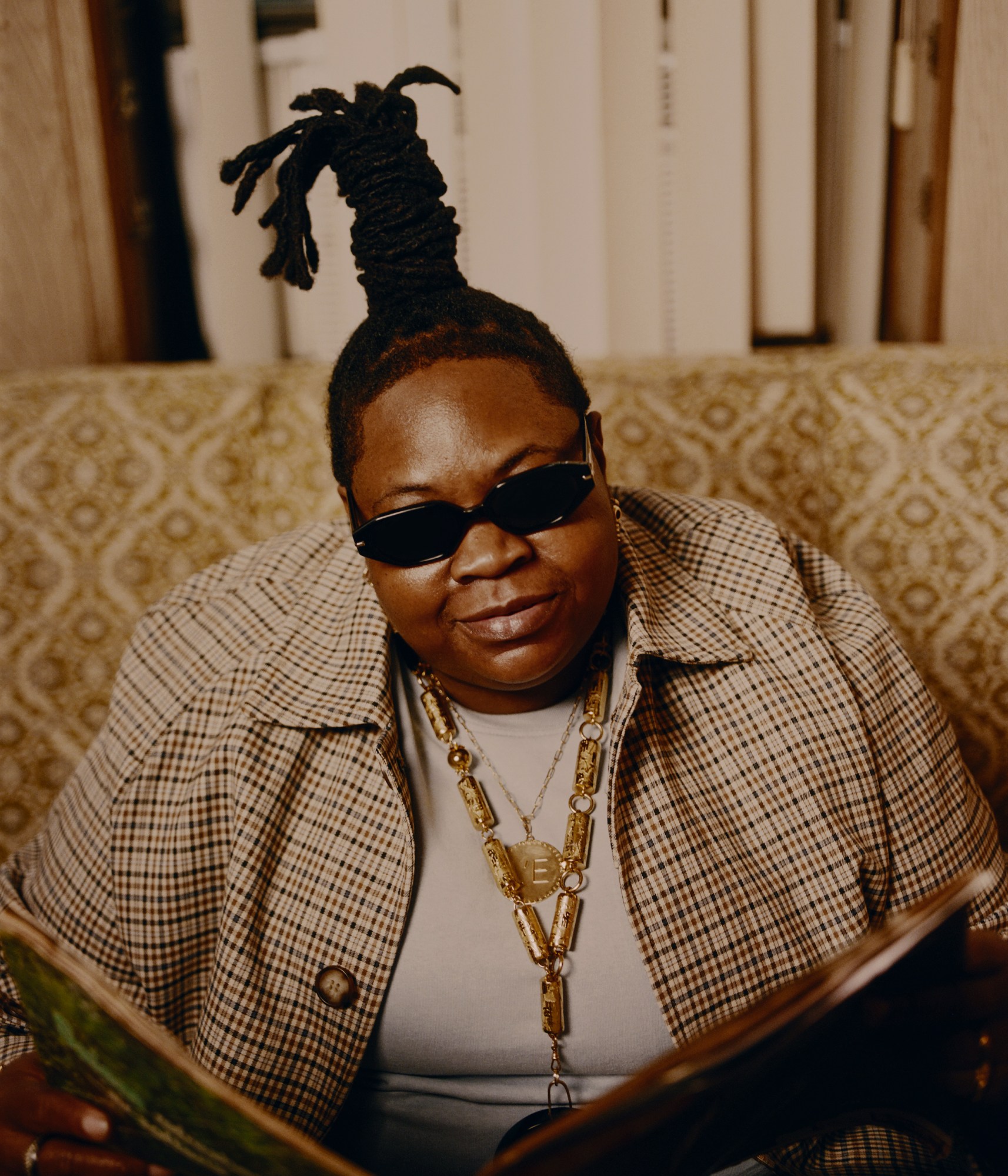 a woman wearing sunglasses and gold jewelry holding an open book photographed by kendall bessent for chucha studios