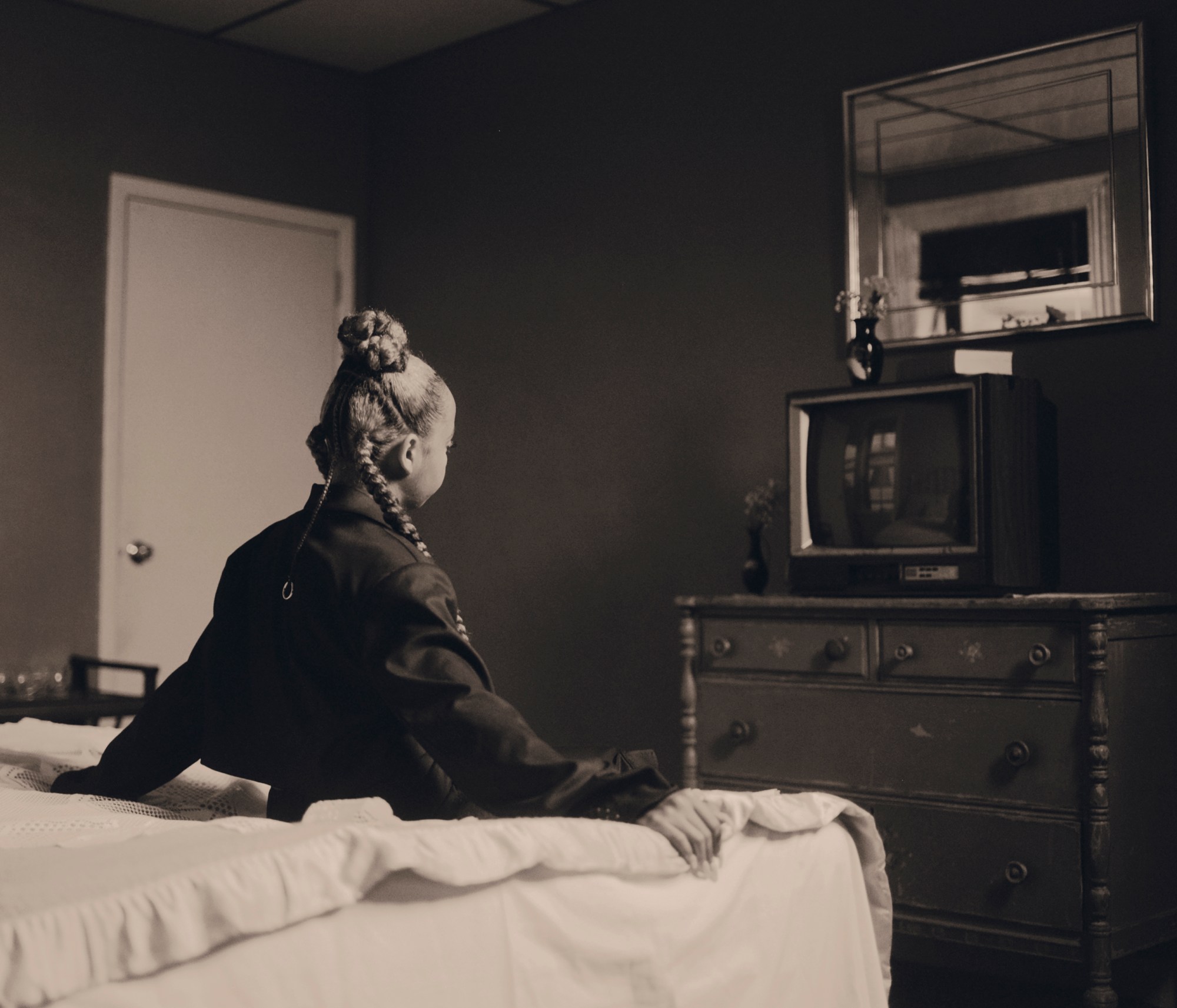 the back of a girl sitting on a bed and staring at a tv photographed by kendall bessent for chucha studios