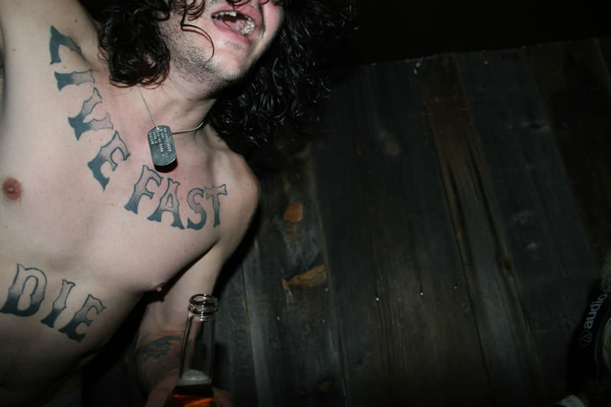 a man with a tattooed chest that says live fast die young photographed by the cobrasnake