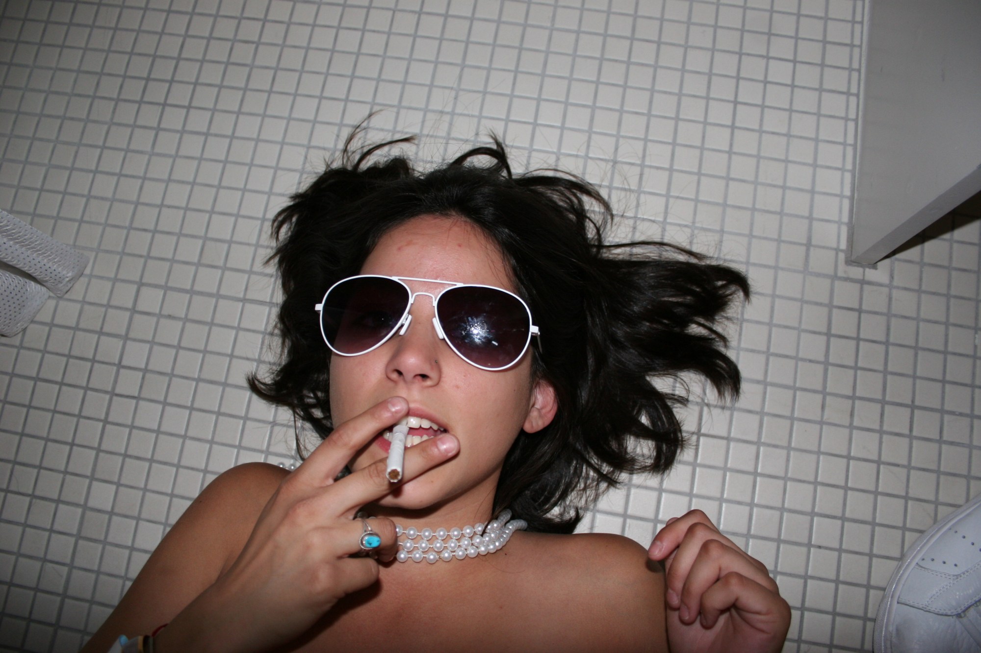 a girl lying on the bathroom floor smoking a cigarette and wearing sunglasses photographed by the cobrasnake