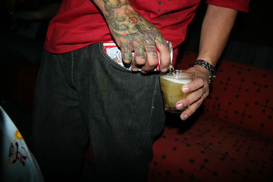 a tattooed man pouring beet into a cup from his pocket photographed by the cobrasnake