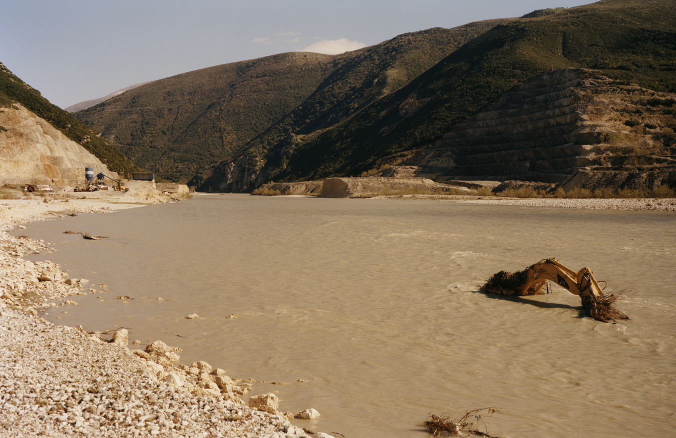 Shallow waters of the river Vjosa in Albania with a machine arm in the ground.