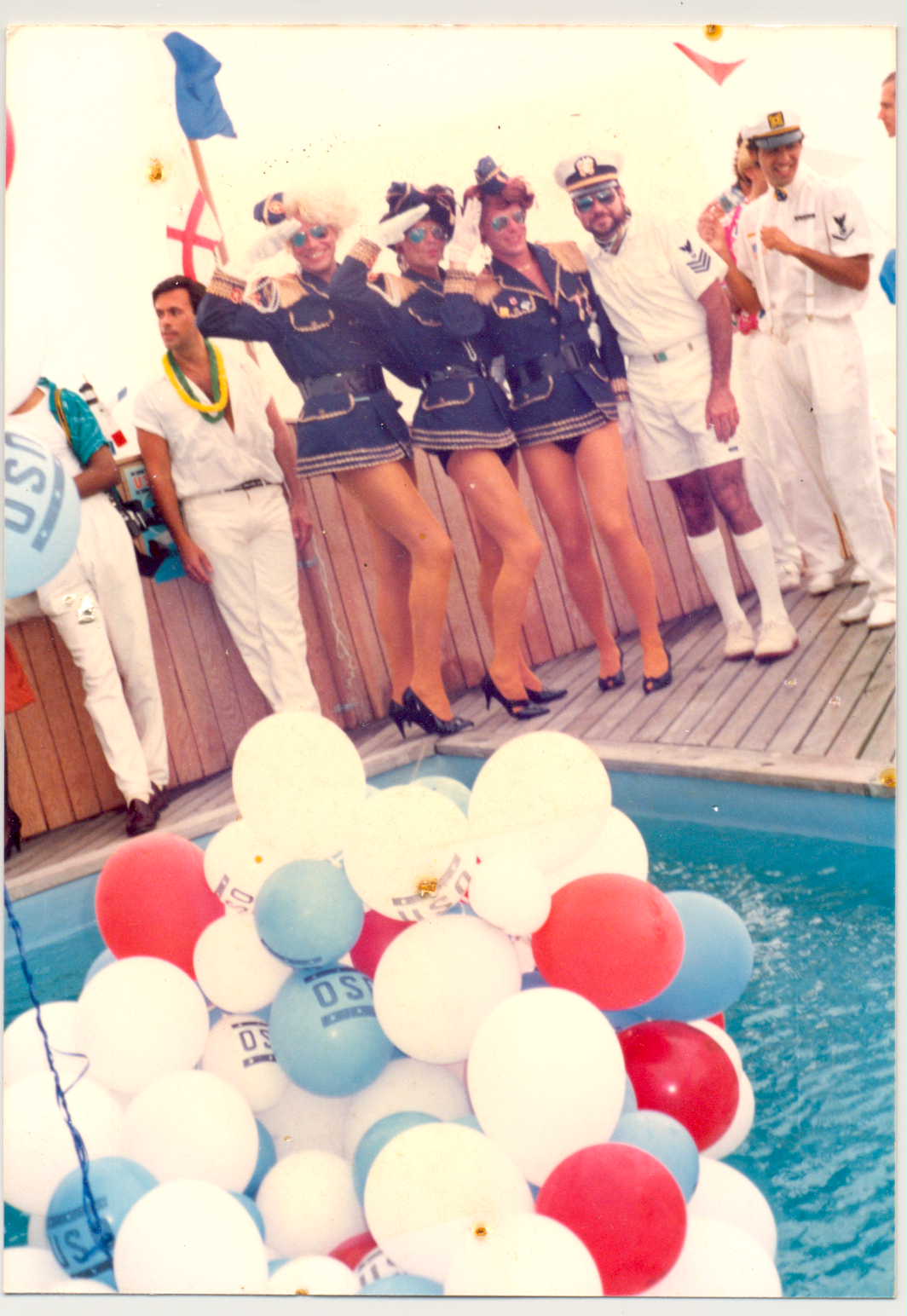 Drag artists dressed as female sailors saluting at a pool party filled with sailors.