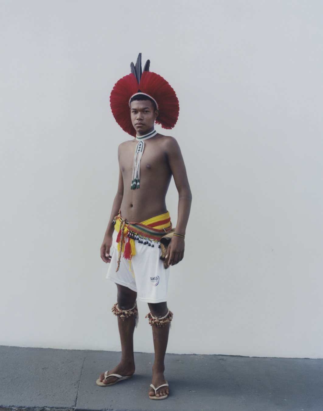 protester wearing shorts and traditional indigenous clothing standing against a wall