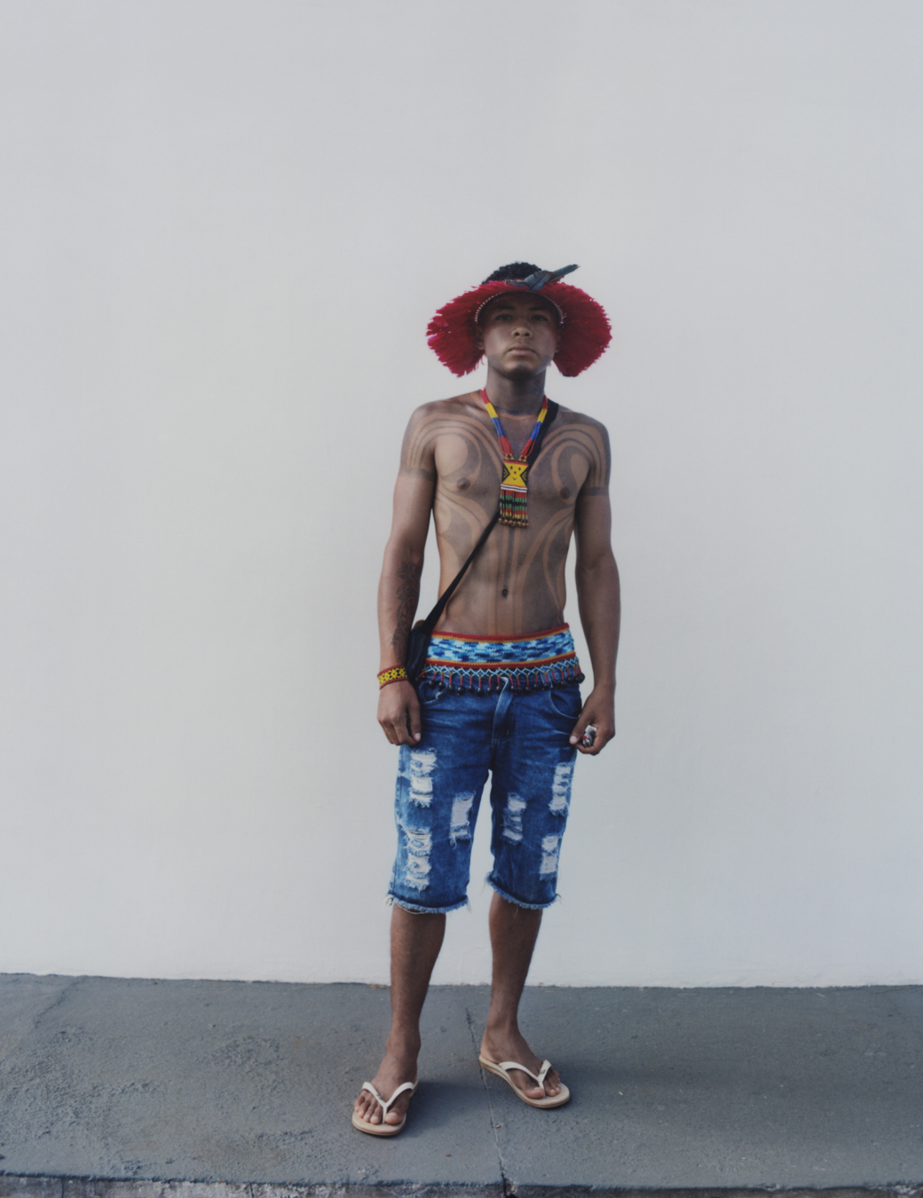 protester wearing denim shorts and traditional indigenous clothing standing against a wall