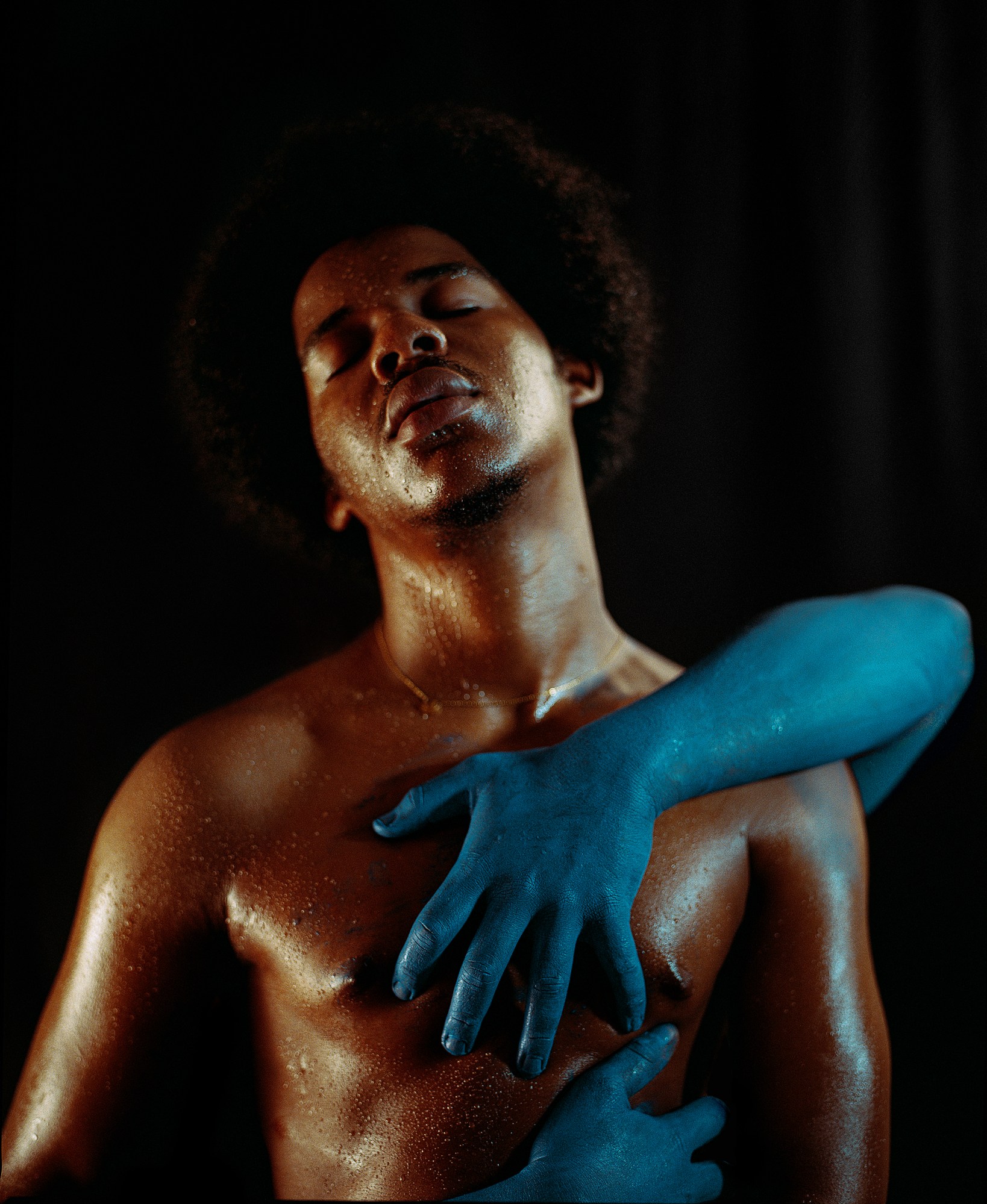 Wet shirtless man with blue arms wrapped around him.