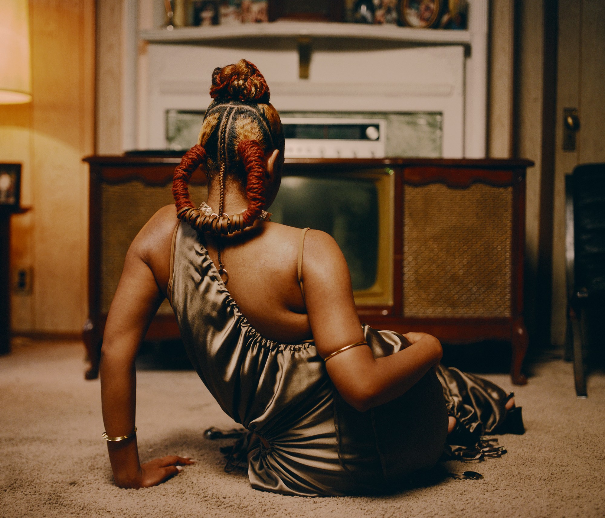 a black woman with her hair braided sits facing an old tv set