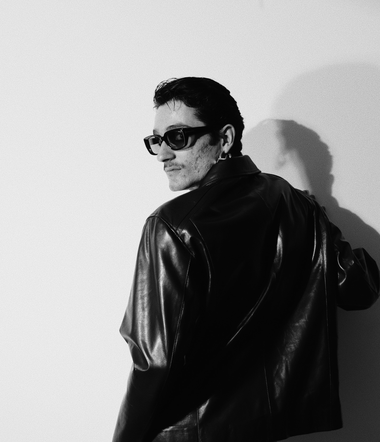 a man wearing a leather jacket and sunglasses looking over his shoulder