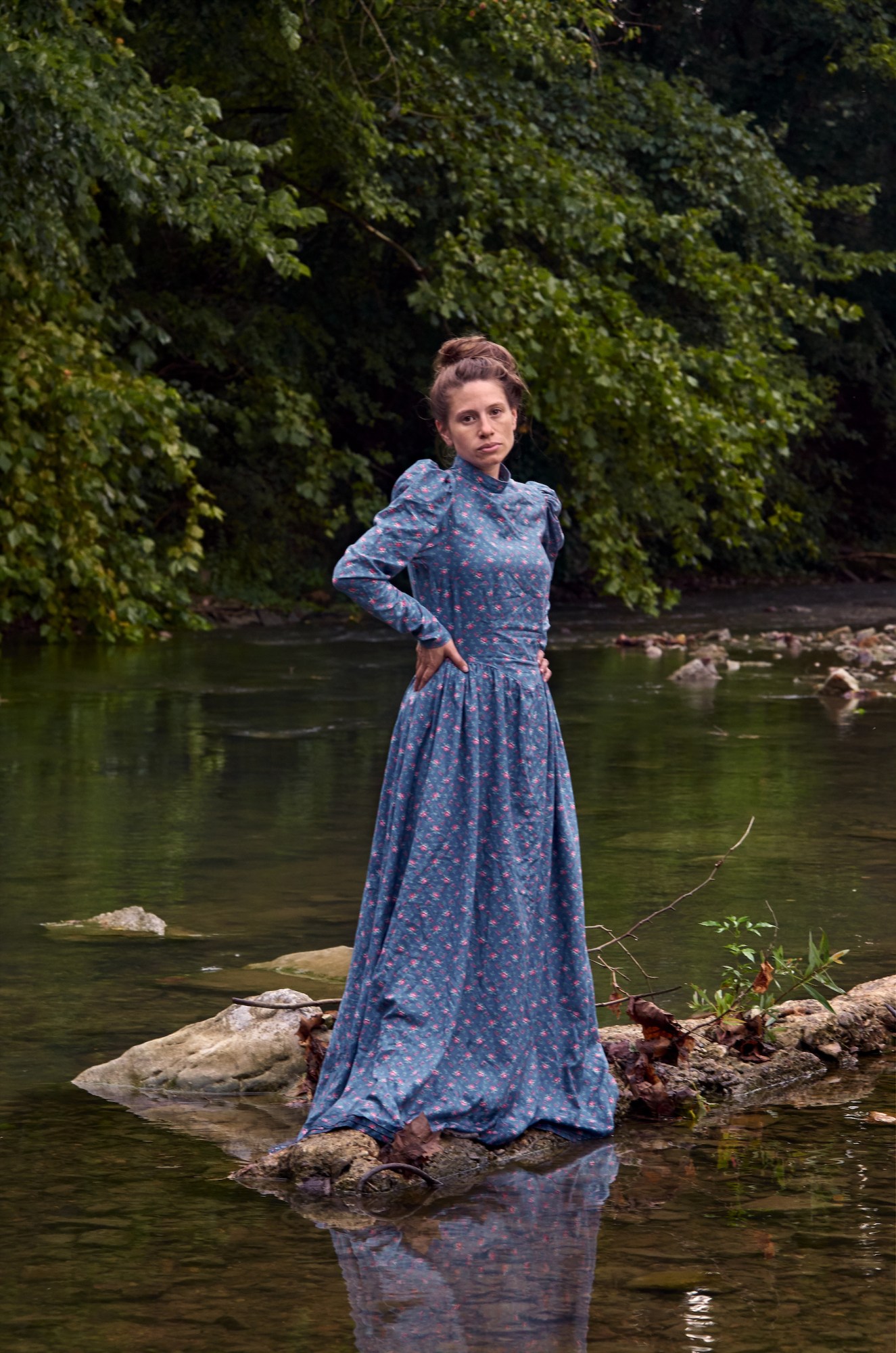 A woman posing in a long dress in a river.