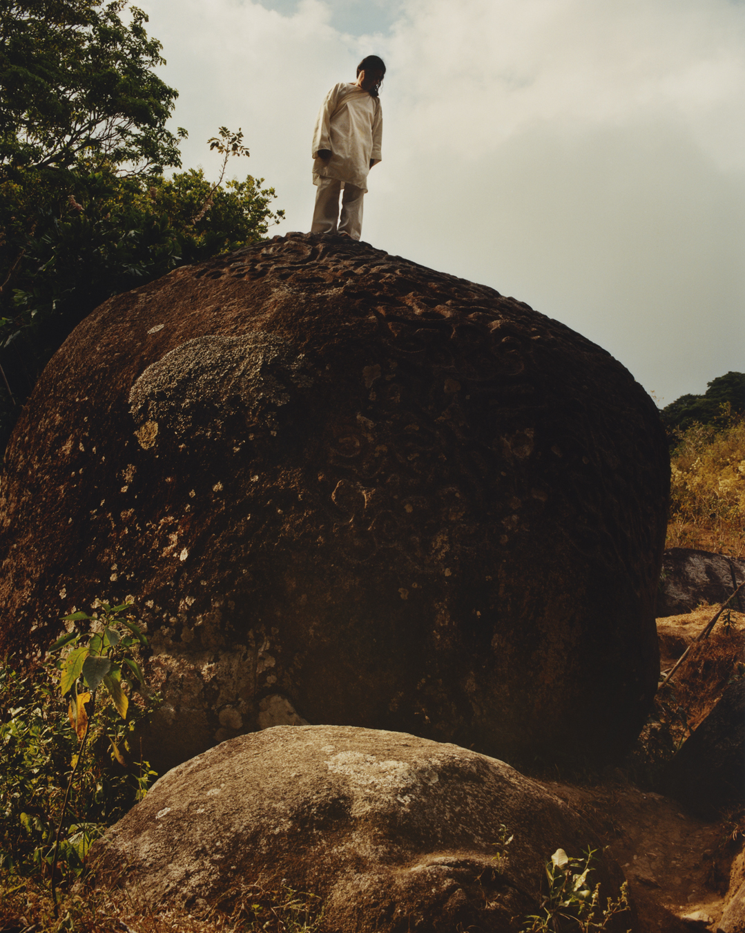 A man stands on top of a large rock in the forest.