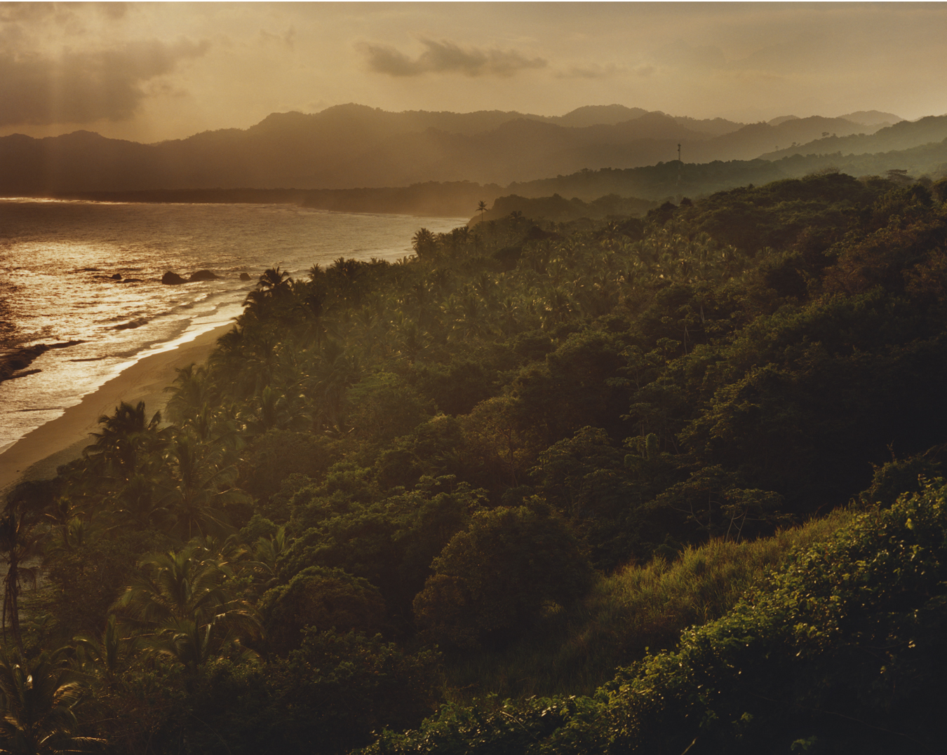 landscape photo overlooking the forests, waters, beach and mountains as the sun sets.