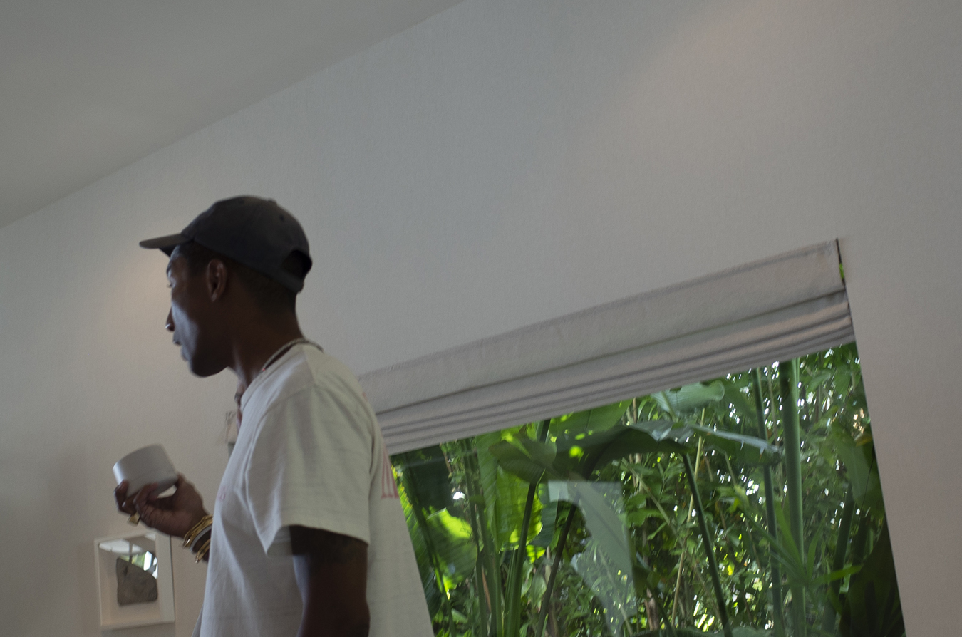 Pharrell Williams holding a Humanrace skin cream and standing by the window.