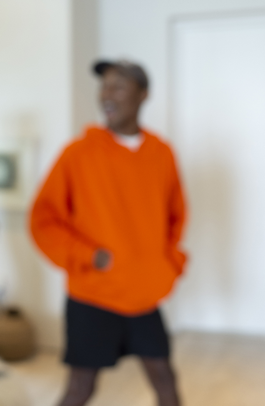 Blurry photograph of Pharrell Williams in an orange hoodie and black shorts