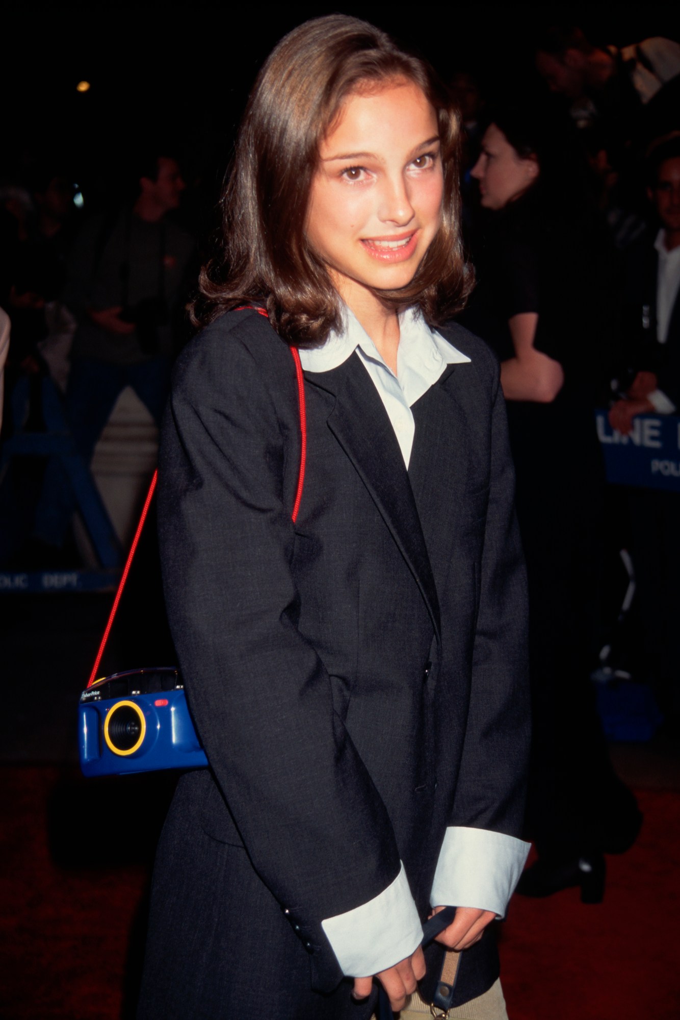 Natalie in an oversized blazer and Polaroid camera hanging from her arm at the premiere of might Aphrodite in 1995.