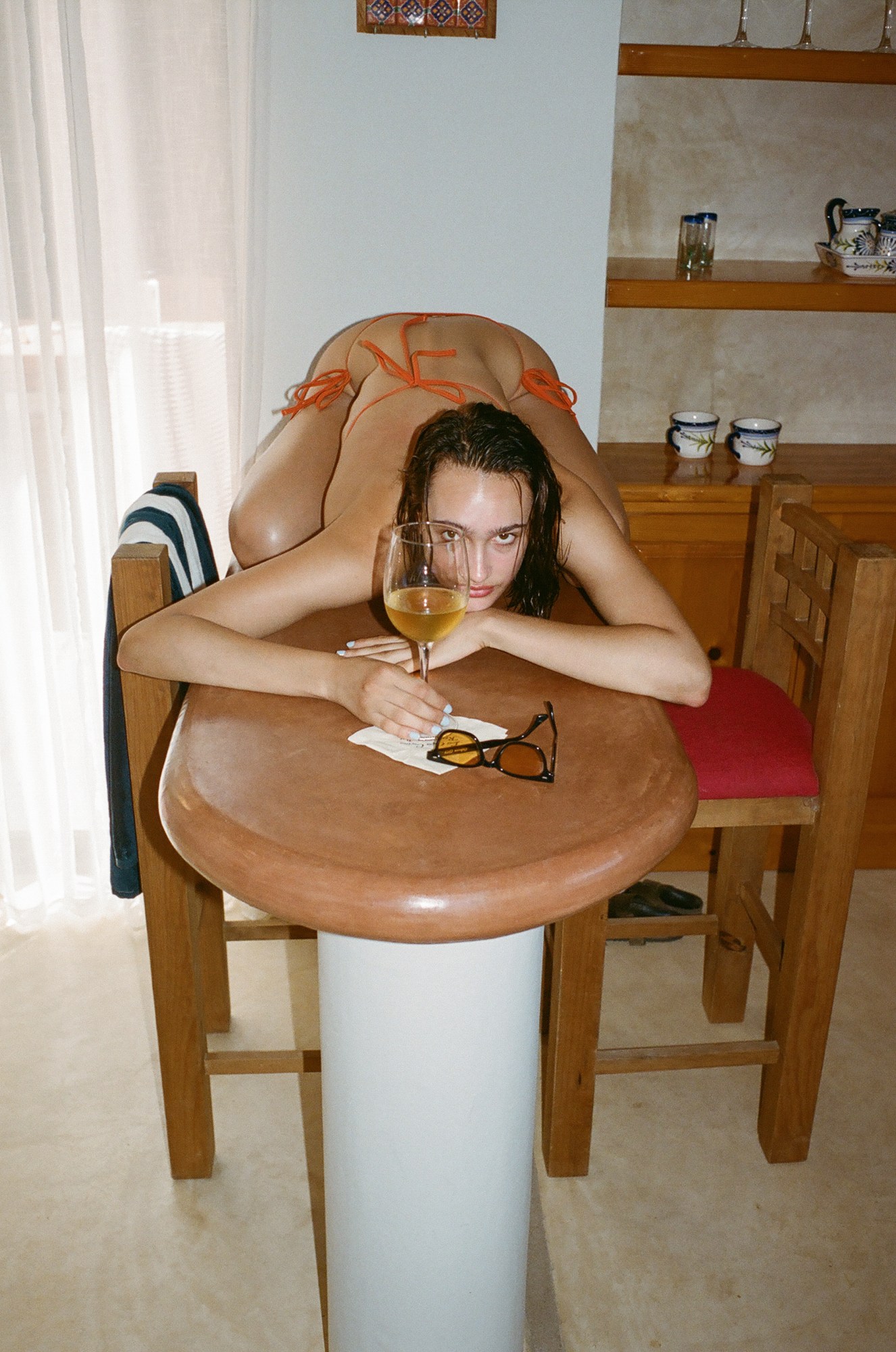 a girl posing on top of a kitchen counter top with a glass of wine