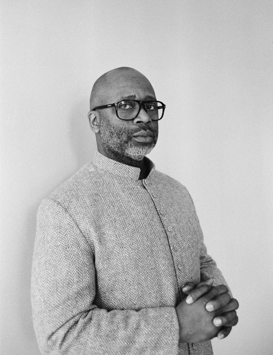 Portrait of Theaster Gates standing against a white wall.