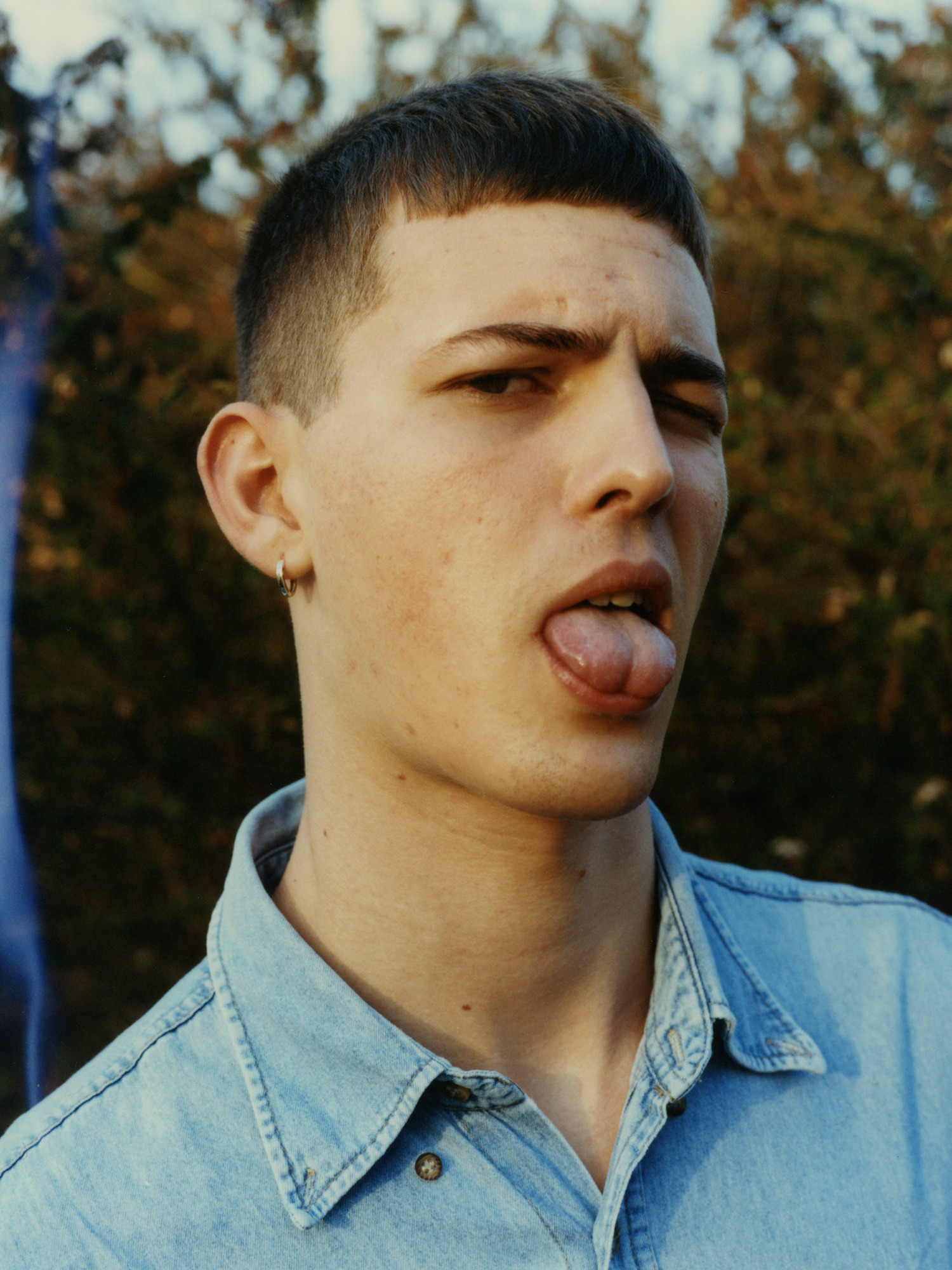 a masc presenting person with an earring and short cropped hair sticks their tongue out to camera