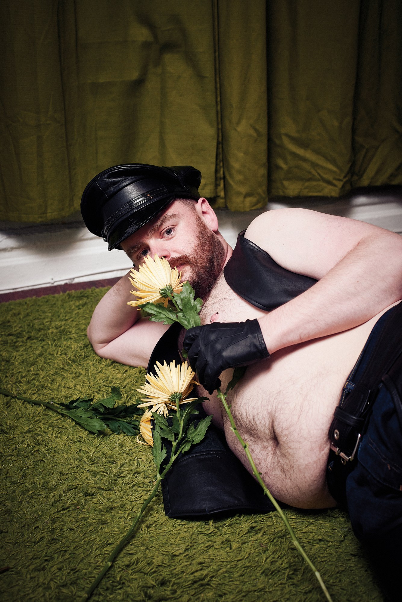 person sniffing flowers wearing jeans and a leather waistcoat, gloves and hat.