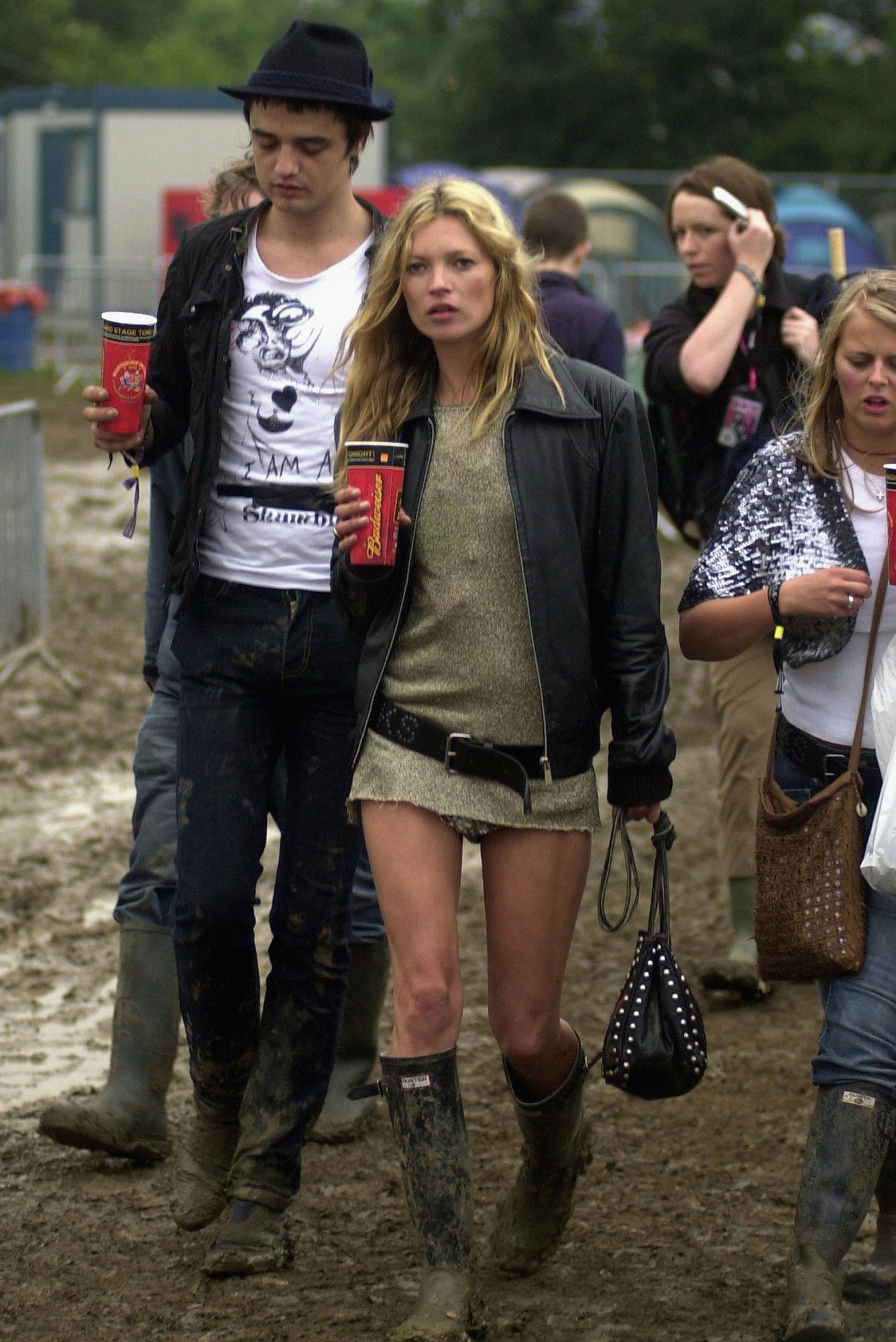 Kate moss in wellies, a belted top and leather jacket with a drink at Glastonbury