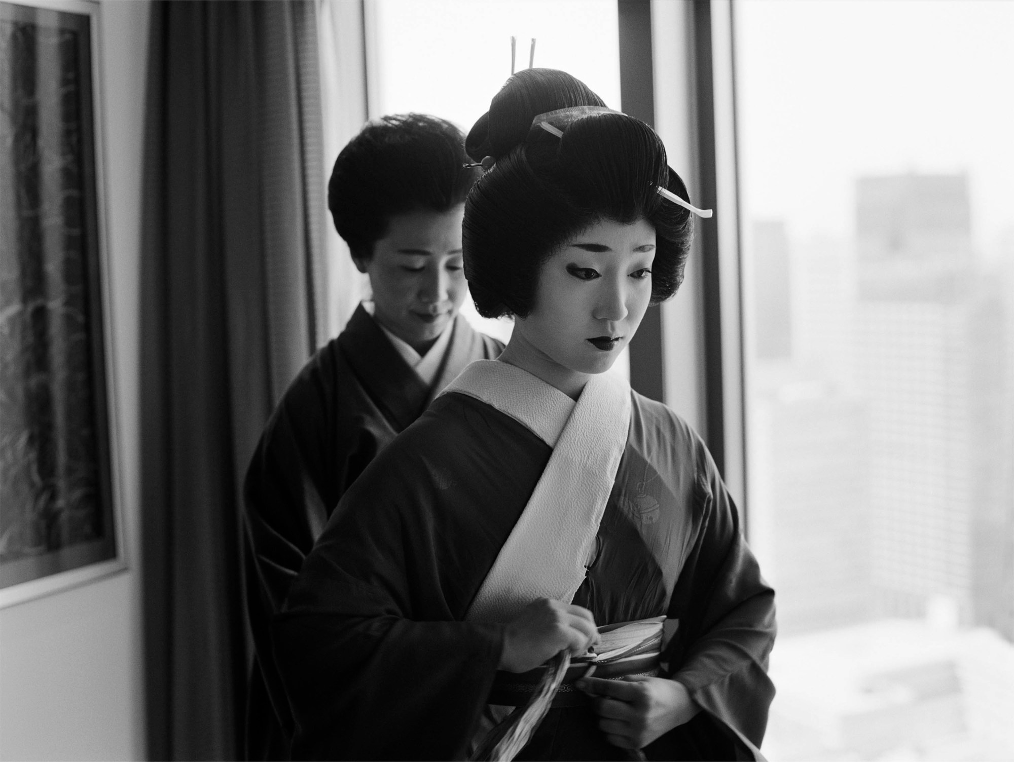 a geisha prepares herself, with an aunt figure helping with her robe