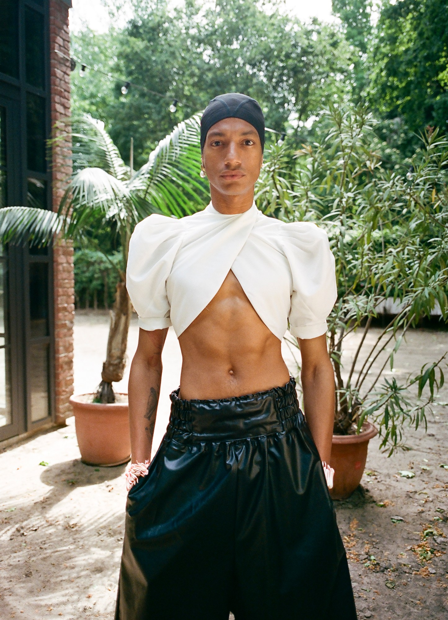 MJ Harper photographed by Rae Tilly standing in a leafy garden wearing pearls and leather trousers