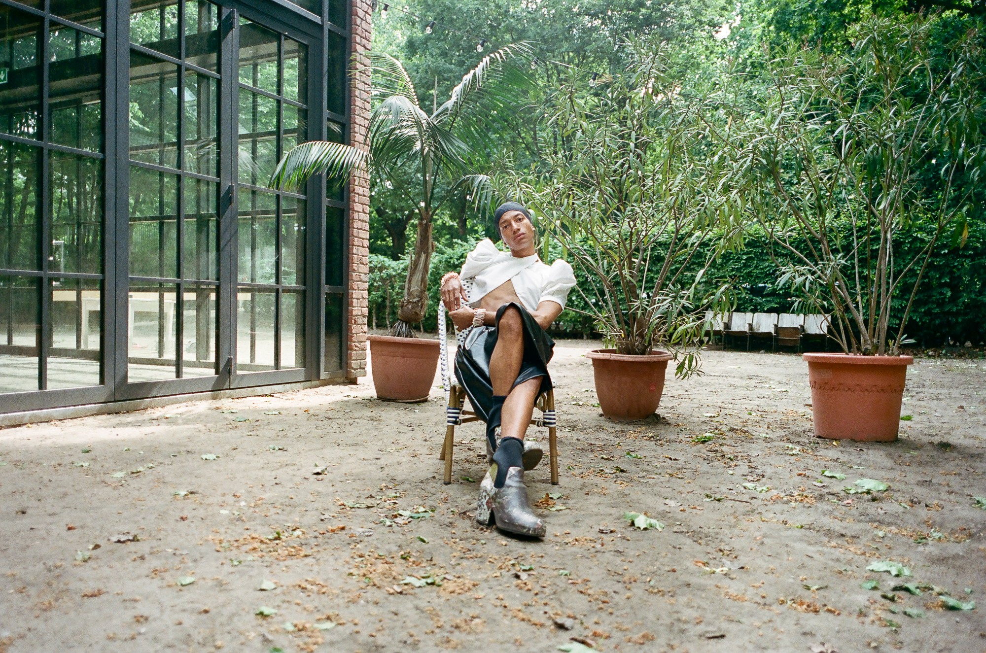 MJ Harper photographed by Rae Tilly sitting with legs crossed on a chair in a garden