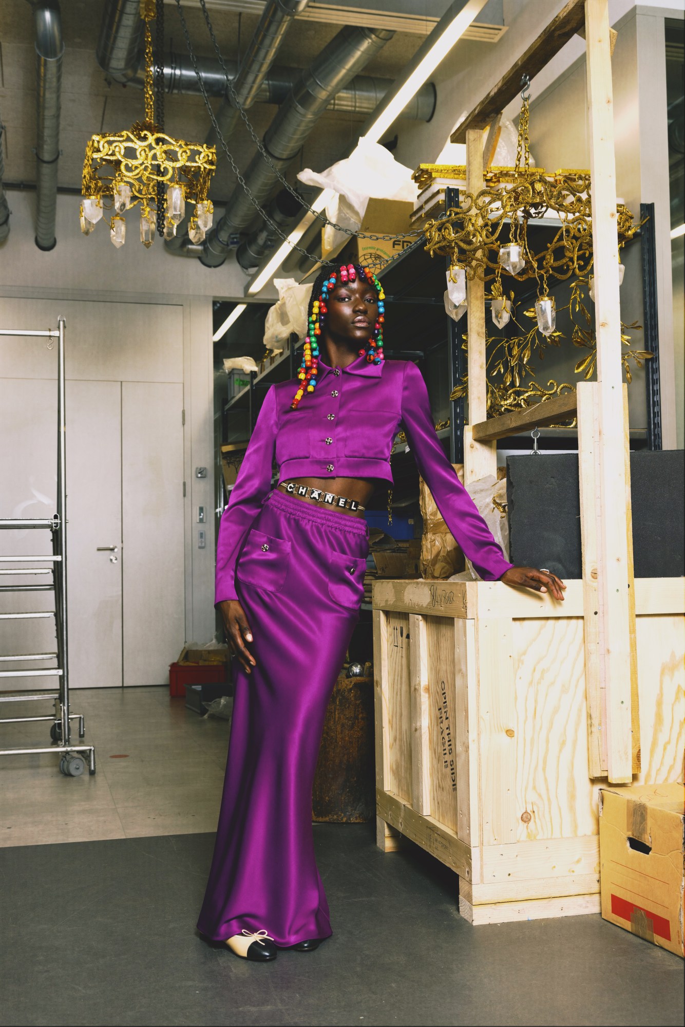 a model wears a bright purple silk skirt suit with large rainbow beads in her braids