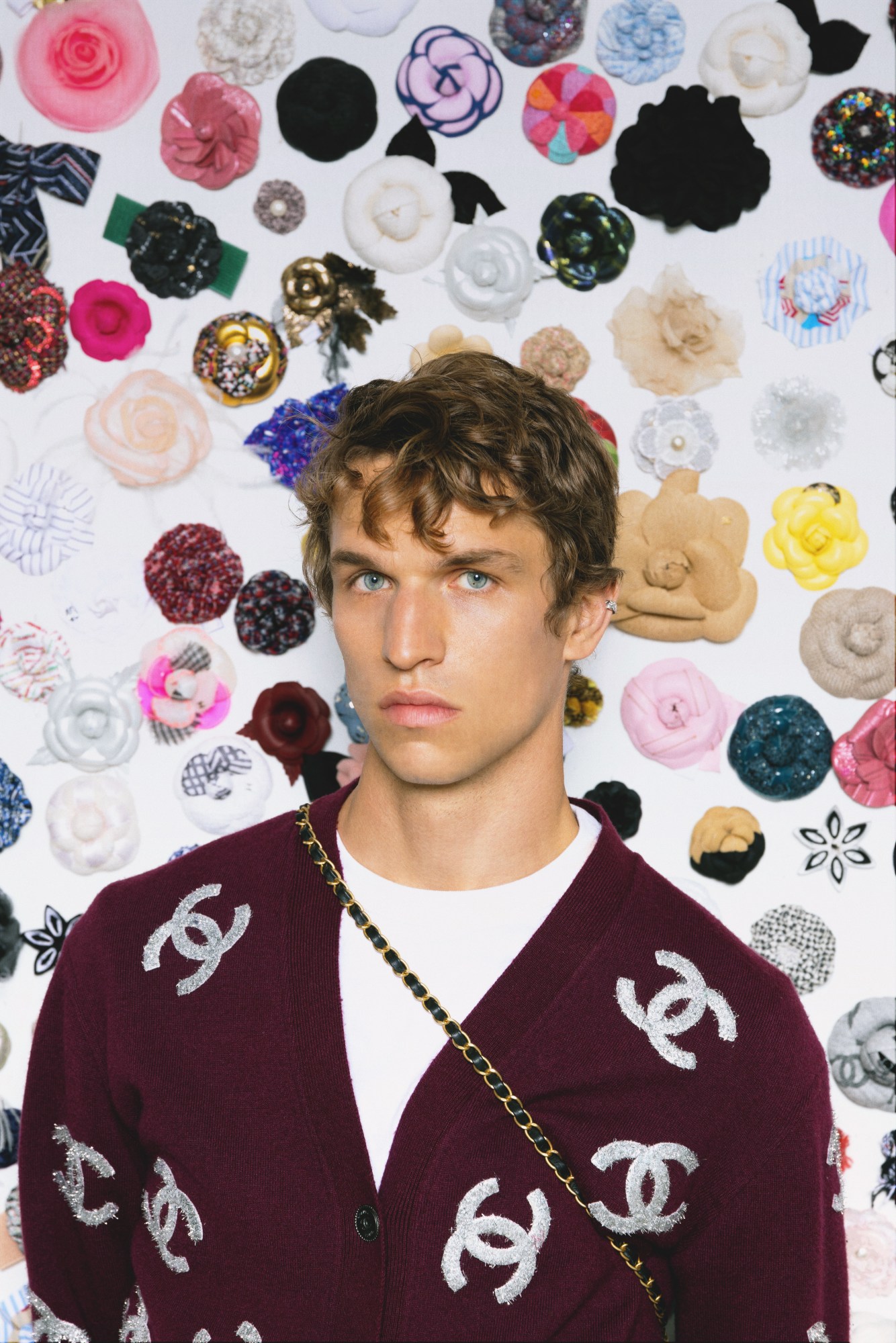 a male model wears a cardigan with chanel logo, standing in front of a wall of textured flowers