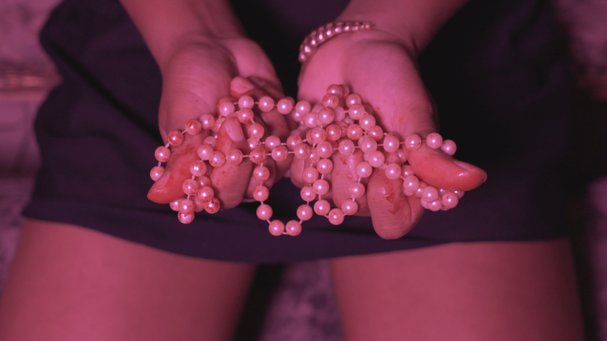 hands holding a bloody pearl necklace over spread legs