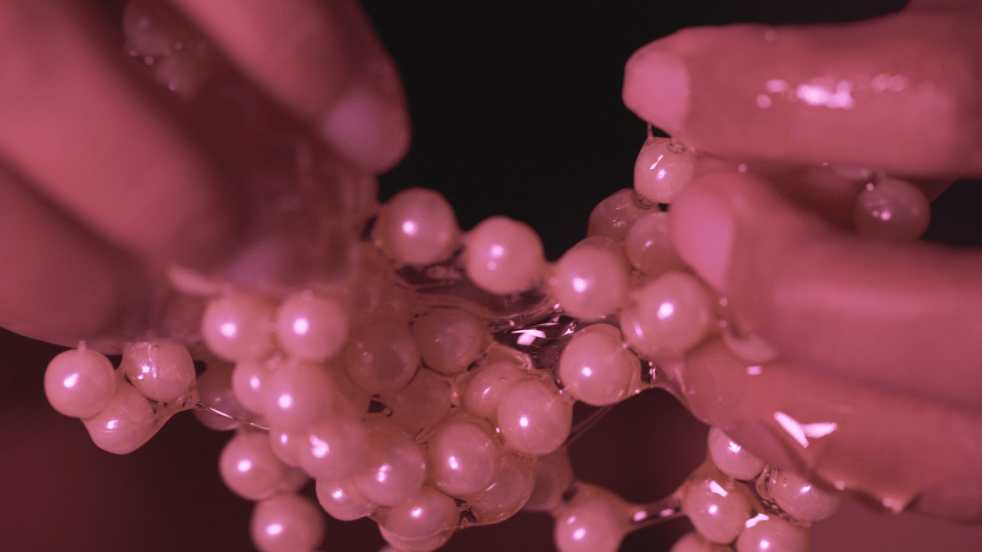 a close up of hands holding pearls in a shiny liquid