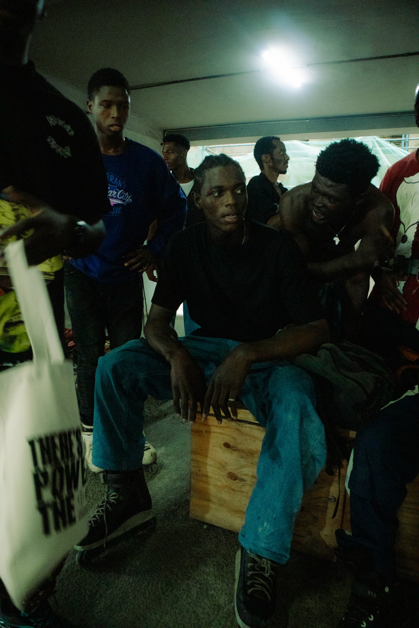 photo of a man sat on a wooden box with other men around him.