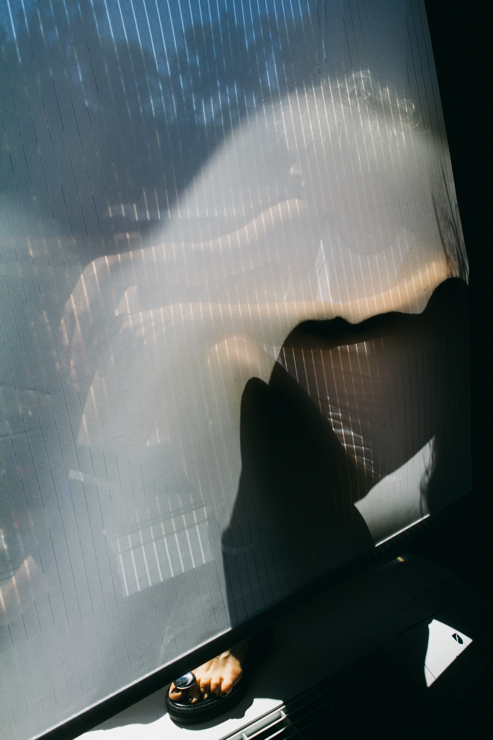 photo of the silhouette of someone sitting on a window sill behind a blind